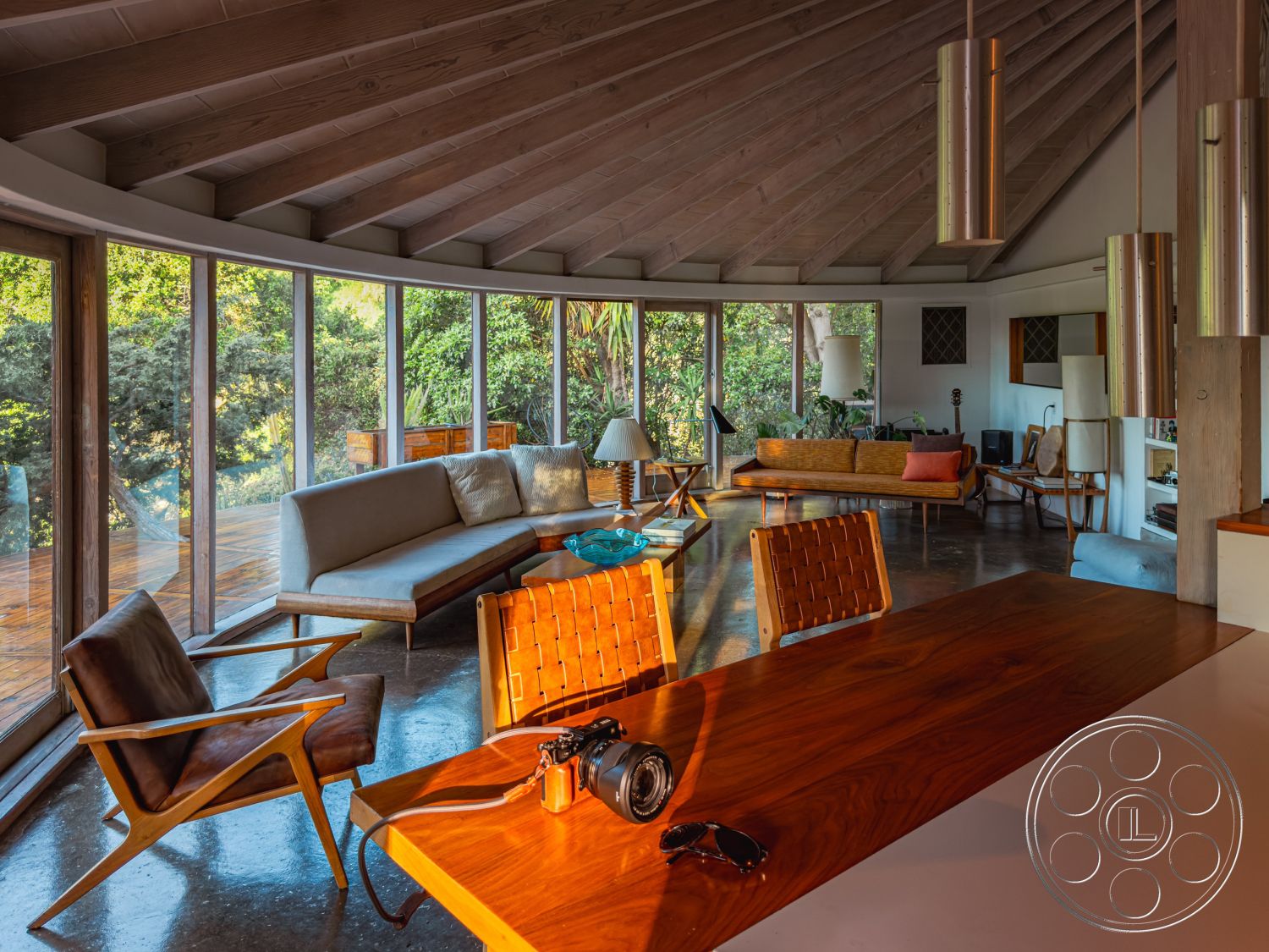 Pad 90210 - natural light interior, exposed wood ceiling beams interior, floor-to-ceiling windows interior, wood paneling interior, wooden dining table interior, concrete floor interior, mid-century modern architectural style interior, round coffee table interior, open-concept living area interior, curved sofa interior, outdoor deck view interior, minimalist furniture interior, tropical garden view interior, modern pendant lights interior, sculptural armchair interior