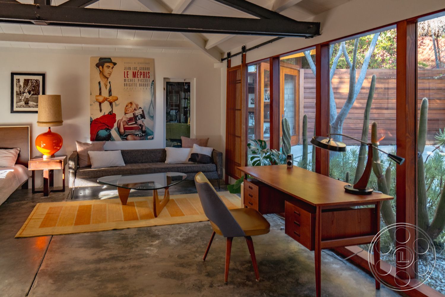 Pad 90210 - open floor plan, modern coffee table, decorative wall art, casual seating area, mid-century modern decor, retro design, colorful area rug, framed art prints, exposed wood ceiling beams, textured fabric sofa, interior concrete flooring, glass wall panels, natural light source, orange ceramic lamp, cactus indoor plants, walnut wood desk, modernist styling