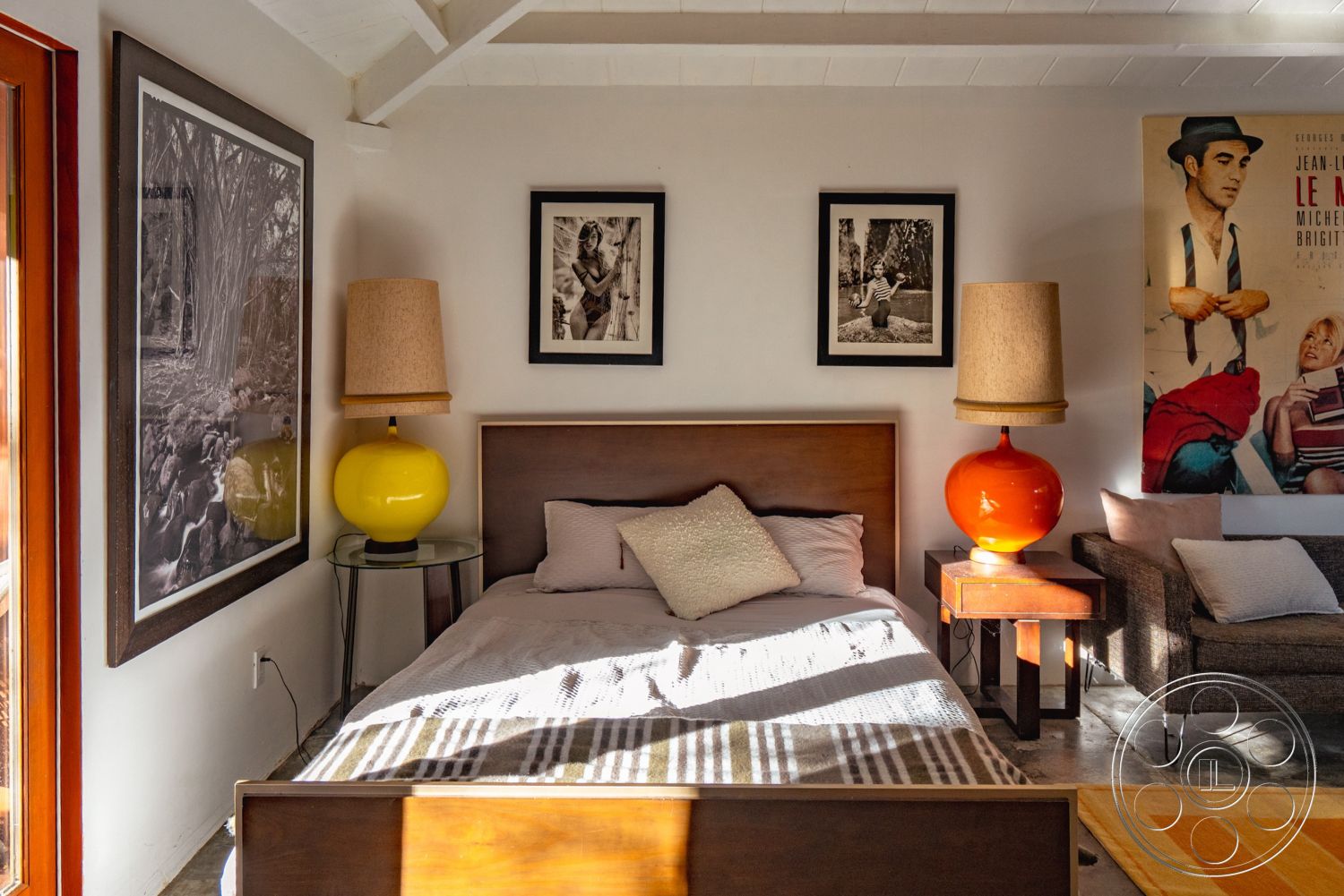 Pad 90210 - artistic wall decor, textured throw pillows, dark wooden bed frame, exposed wood ceiling beams, glass partition walls, interior bedroom design, natural light illumination, white painted walls, concrete floor finish, hardwood bedroom flooring, cozy indoor setting, contemporary accent chair, modern two-person bed, yellow glass lamp, orange glass lamp, vintage style artwork