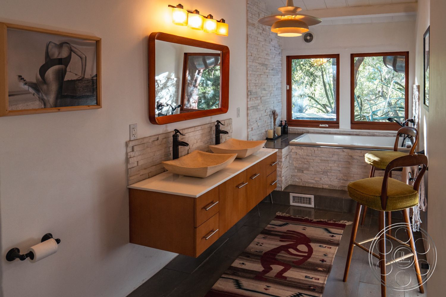 Pad 90210 - minimalist decor, exterior, glass shower enclosure, dark slate flooring, contemporary bathroom design, white painted walls, urban forest setting, natural stone accent wall, floating vanity with natural wood finish, double basin sink with sculptural bowls, large window view of nature, retro pendant lighting, wood-framed mirror, colorful tribal area rug, wooden accent chair with green upholstery, bathtub with stone surround