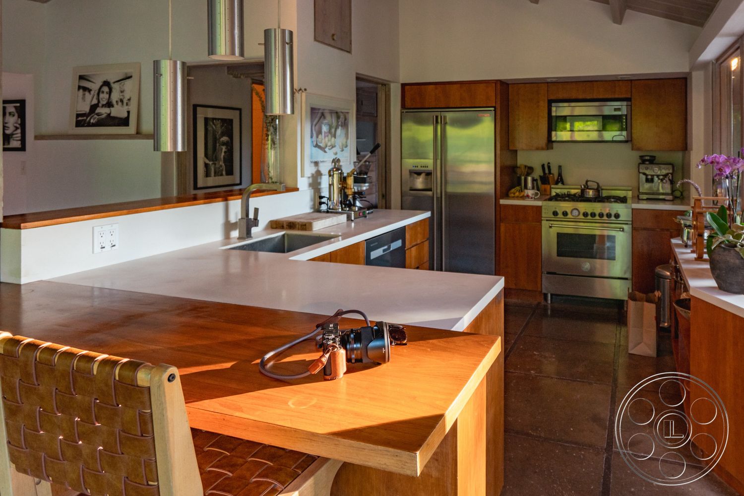 Pad 90210 - modern pendant lighting, natural light from large windows, stainless steel kitchen appliances, minimalist kitchen decor, high ceilings with exposed wood beams, open concept kitchen layout, wood cabinetry with natural finish, contemporary home office area, kitchen island with seating, white quartz kitchen countertop, concrete wall texture, bright and airy kitchen ambiance, exterior kitchen with large windows, concrete kitchen flooring, wall-mounted shelves for art display, tile backsplash behind cooking area, integrated refrigerator design, leather woven bar stools, suburban residence with garden view