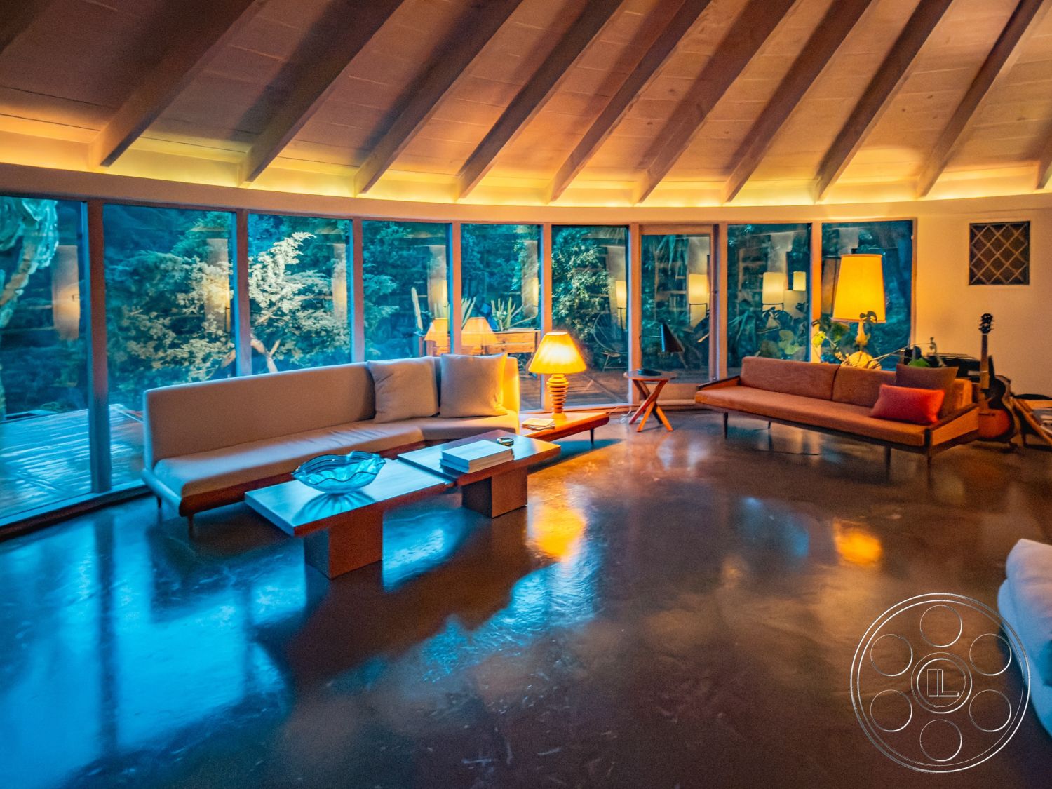 Pad 90210 - warm color palette, soft ambient lighting, minimalist coffee table, cozy reading nook, plant-filled environment, integrated indoor-outdoor flow, natural light-filled space, open floor plan layout, exposed wooden ceiling beams, glass wall windows, interior concrete polished floor, mid-century modern living room, wooden framed furniture, curved room design, contemporary sofa design