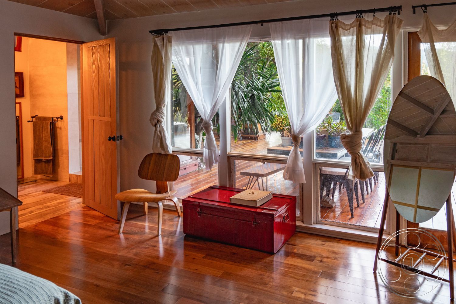 Pad 90210 - interior recessed lighting, interior textured wall finish, interior minimalist decor, exterior wood deck, exterior sliding glass doors, interior open floor plan, interior hardwood bedroom flooring, interior warm color palette, exterior potted plants, interior round mirror, interior simple wooden chair, interior sheer curtain window treatments, exterior natural light, interior casual dining area, interior wood panel door, interior red storage trunk, interior bathroom access