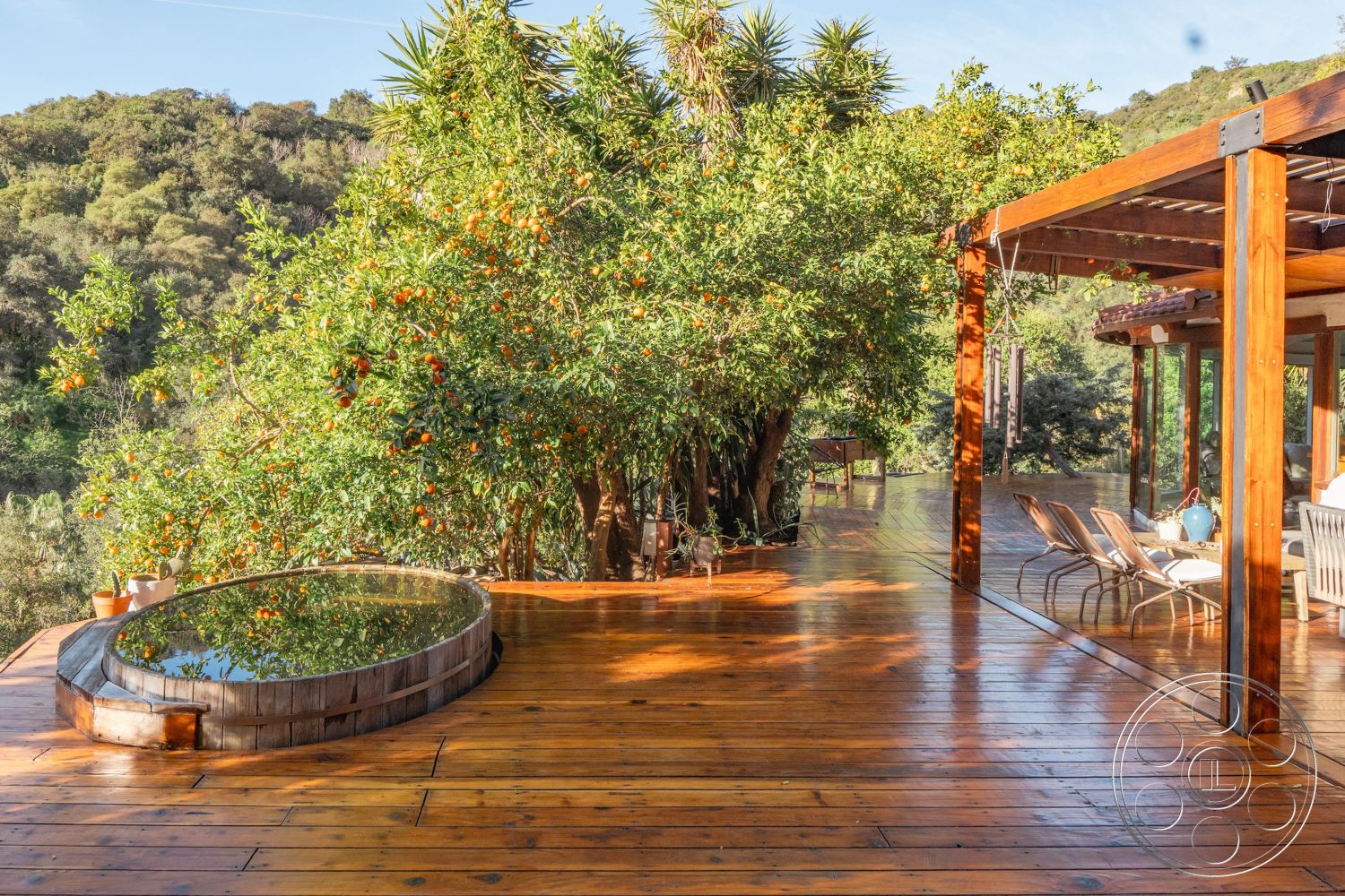 Pad 90210 - exterior, sustainable materials, open outdoor space, mountain view setting, wooden deck flooring, floor-to-ceiling glass walls, rustic outdoor ambiance, natural landscape integration, modern pergola structure, circular wood hot tub, surrounding orange tree, wooden patio seating, orange grove surroundings
