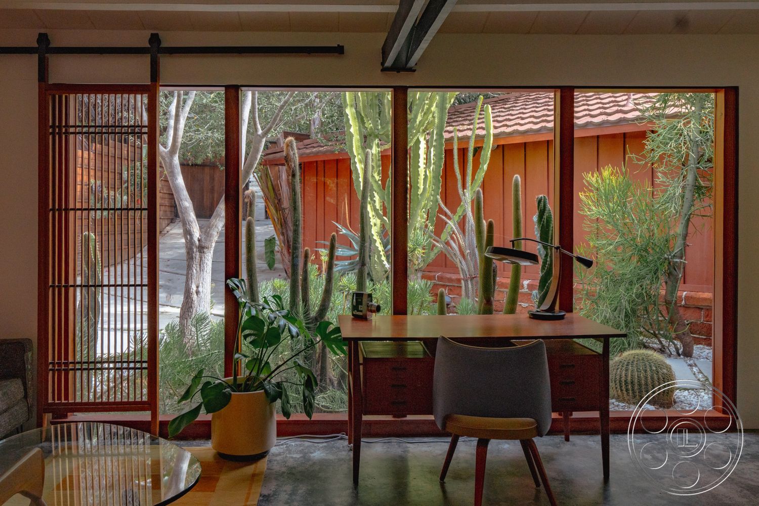 Pad 90210 - minimalist decor, polished concrete floor, concrete flooring, exposed wooden beams, landscaped garden view, green indoor plants, sliding glass door, wooden window frames, textured wall treatments, natural light interior, open interior layout, contemporary workspace, mid-century modern desk, brick exterior wall, urban desert setting, desert plant accents, cactus garden view, wood slat privacy screen, scandinavian chair design