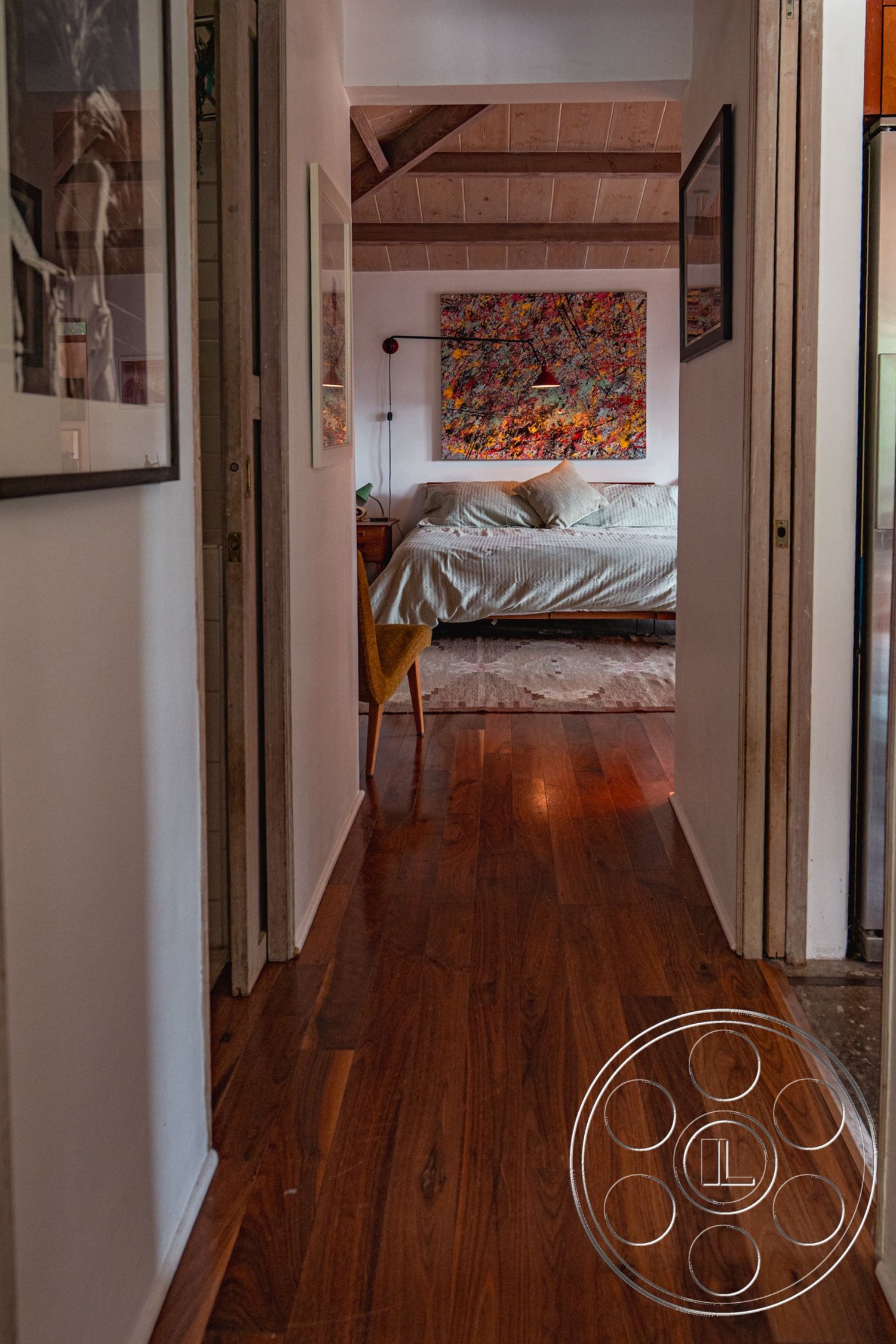 Pad 90210 - minimalist decor, open concept layout, stylish floor lamp, wooden nightstand, natural light from windows, rugged area rug, exposed wood ceiling beams, hardwood hallway floors, white painted walls, mid-century modern furnishings, modern artwork on walls, cozy bedroom area, textured fabric bed linens