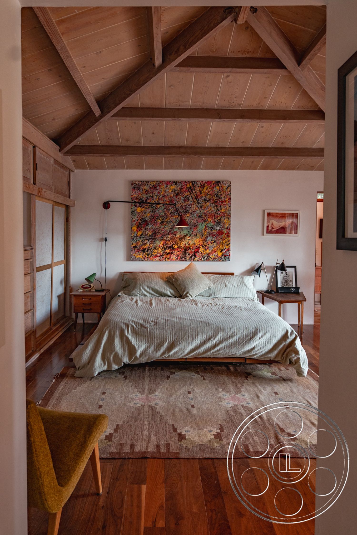 Pad 90210 - natural light, contemporary design, textured area rug, wood frame bed, green accent pillow, exposed wood ceiling beams, cozy bedroom setting, hardwood bedroom floors, colorful abstract wall art, vaulted ceiling interior, plaid bed linens, mid-century modern nightstands, elegant reading lamp, wooden closet doors