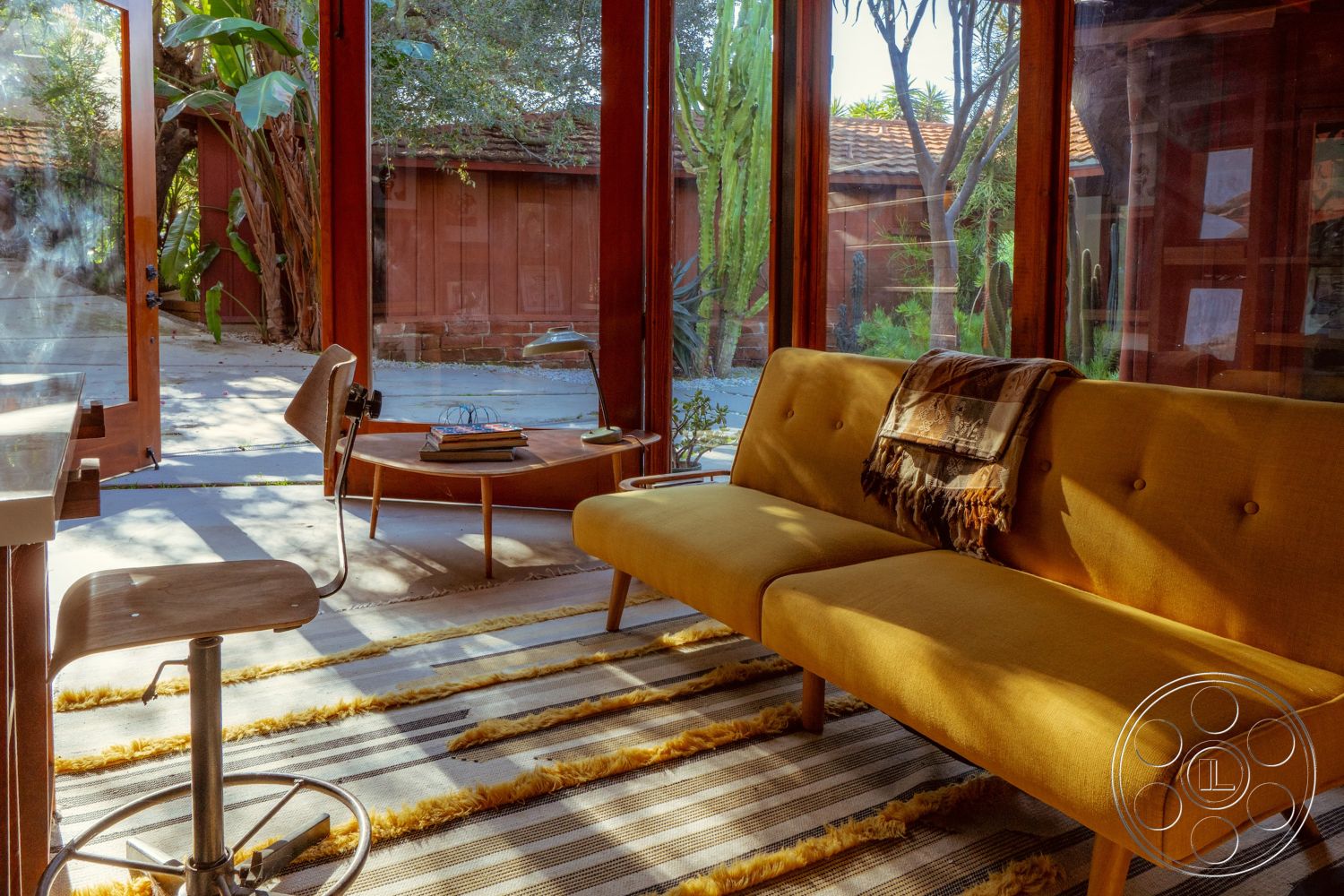 Pad 90210 - minimalist decor, wood coffee table, indoor plants, modern furniture, sliding glass doors, textured wall finishes, soft lighting fixtures, contemporary interior design, open-plan living space, exposed wood beam ceiling, natural light emphasis, floor-to-ceiling glass walls, wood frame structure, yellow upholstered mid-century modern sofa, striped area rug with wood accents, surrounding desert landscaping