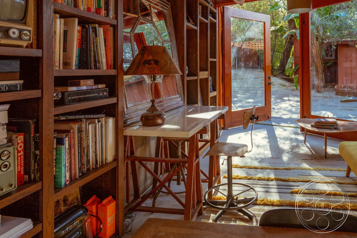 Pad 90210 - neutral color palette, open floor plan, soft area rug, decorative lamp, natural light from large windows, textured wall finishes, mid-century modern furniture, indoor-outdoor living, cozy reading nook, glass patio doors, geometric window shapes, exposed wood ceiling beams, interior wooden bookshelves, marble side table top, rustic hardwood floor