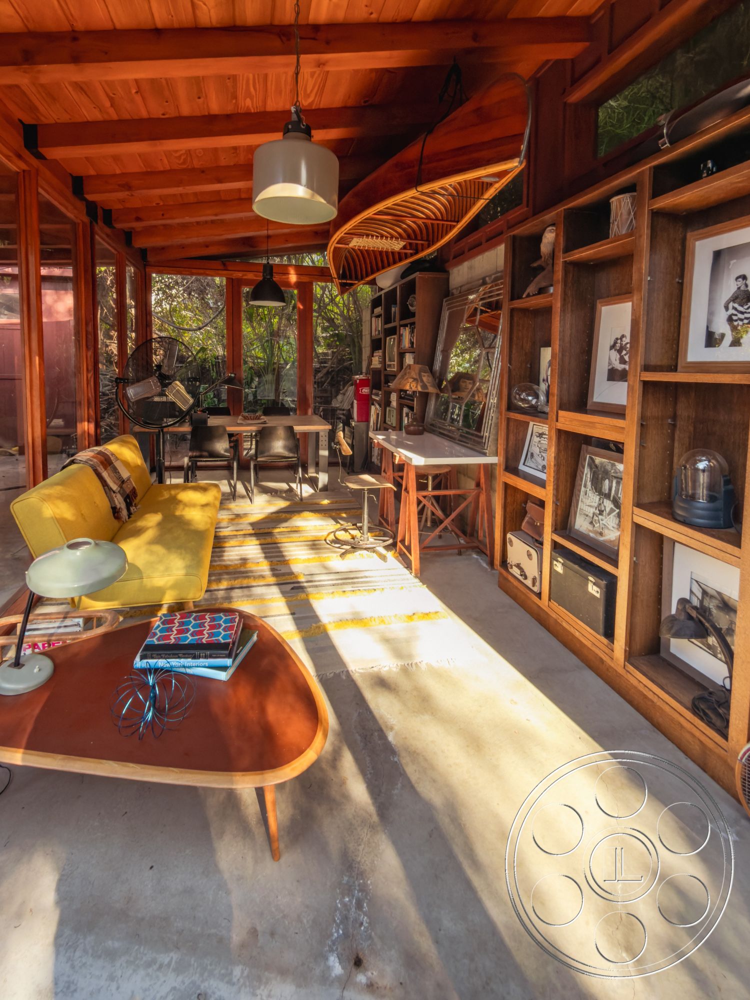 Pad 90210 - concrete floor, modern pendant lighting, interior space, decorative wall art, open living space, mid-century modern design, wooden shelving units, exposed wood ceiling beams, relaxed seating arrangement, yellow upholstered sofa, natural light with large windows, surrounding garden view, industrial-style furnishings, retro coffee table, casual workspace area