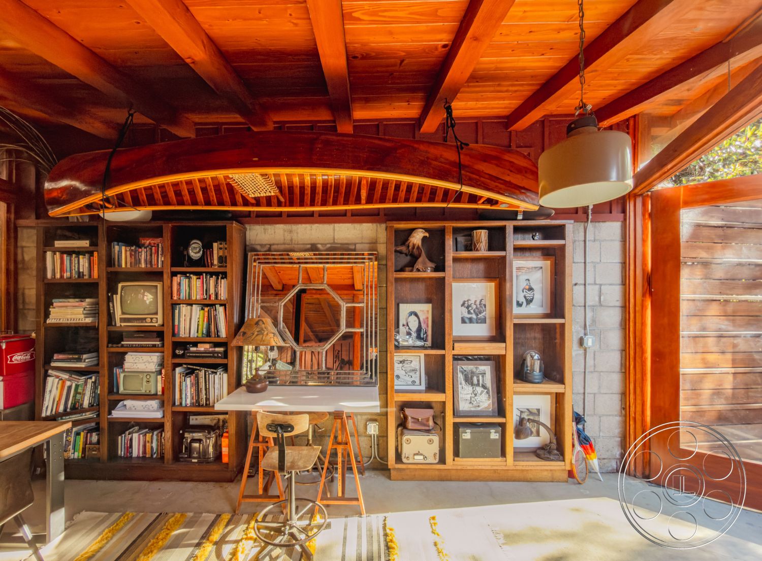 Pad 90210 - neutral color palette, textured area rug, artistic wall decor, contemporary pendant lighting, exposed concrete walls, natural light from large windows, rustic design elements, inviting ambiance, cozy workspace, comfortable seating area, wooden shelving unit, interior wooden beam ceiling, creative storage solutions, metal desk with wooden accents, vintage books on shelves, octagonal mirror feature, hardwood floor area, spacious reading nook, decorative canoe display, functional home office layout