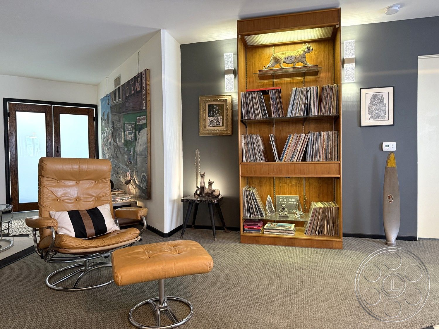 Studio 45 - interior framed artwork, interior leather lounge chair, interior chrome base ottoman, interior wooden record shelf, interior vinyl record collection, interior textured carpet flooring, interior gray accent wall, interior wood framed glass doors, interior ambient wall lighting, interior decorative animal figurine