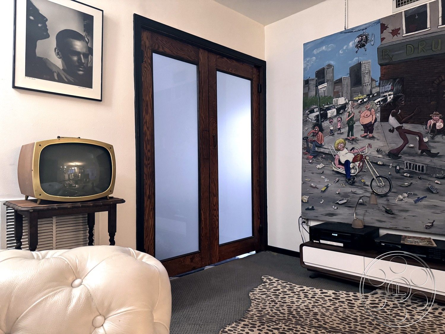 Studio 45 - open floor plan, carpet flooring, urban apartment setting, mid-century modern furniture style, white-painted walls, wooden sliding glass doors, framed black and white portrait photography wall art, vintage television set, wooden side table with turned legs, leather tufted armchair, leopard print area rug, abstract urban art canvas