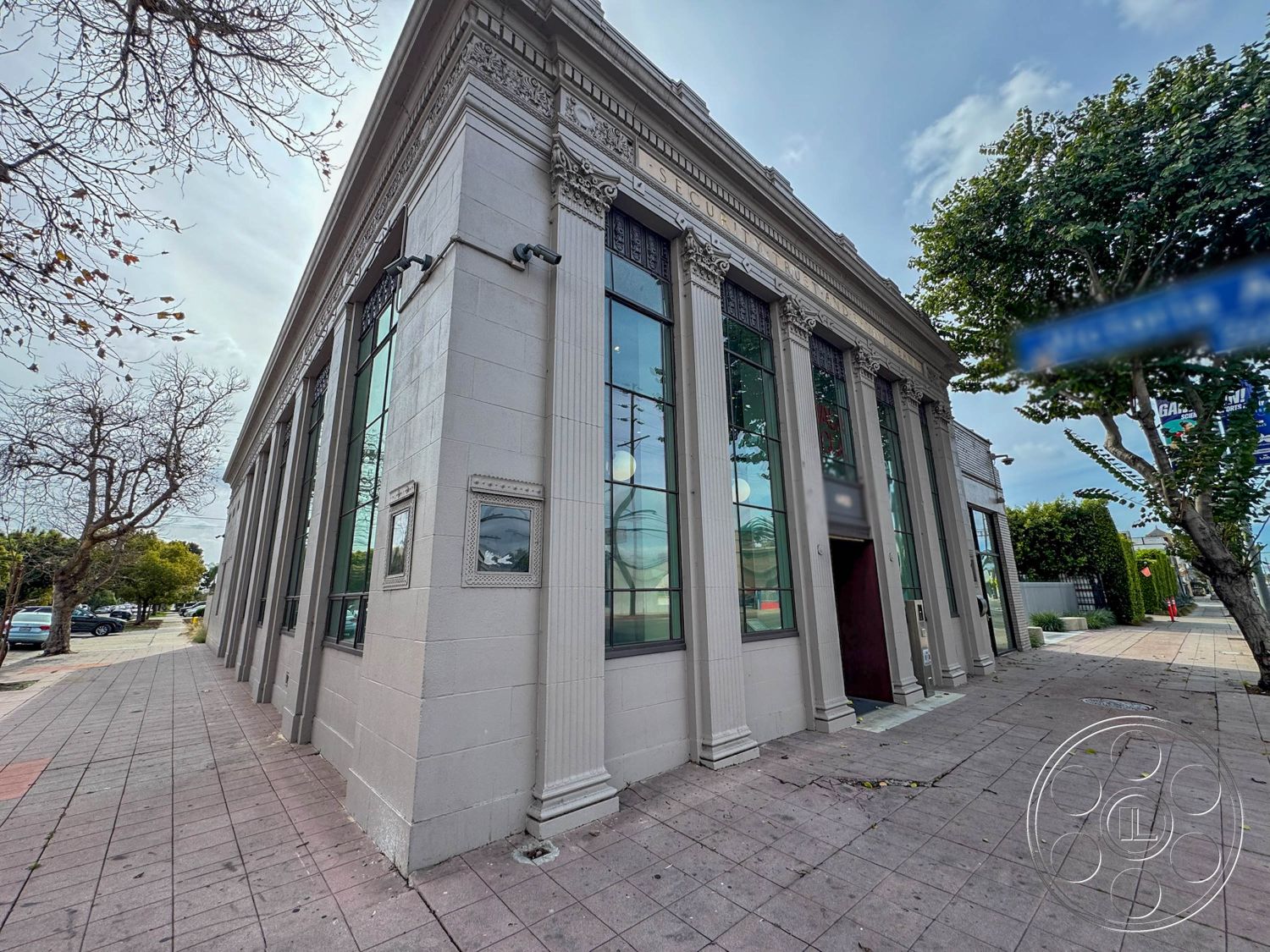 Studio 101 - exterior, large glass windows, textured wall finish, concrete facade, flat roof design, city environment, urban street setting, landscaped front area, ornate cornice details, neoclassical architectural style, decorative pilasters, tall entrance door, window surrounds with moldings, sidewalk with paver stones, trees lining the walkway