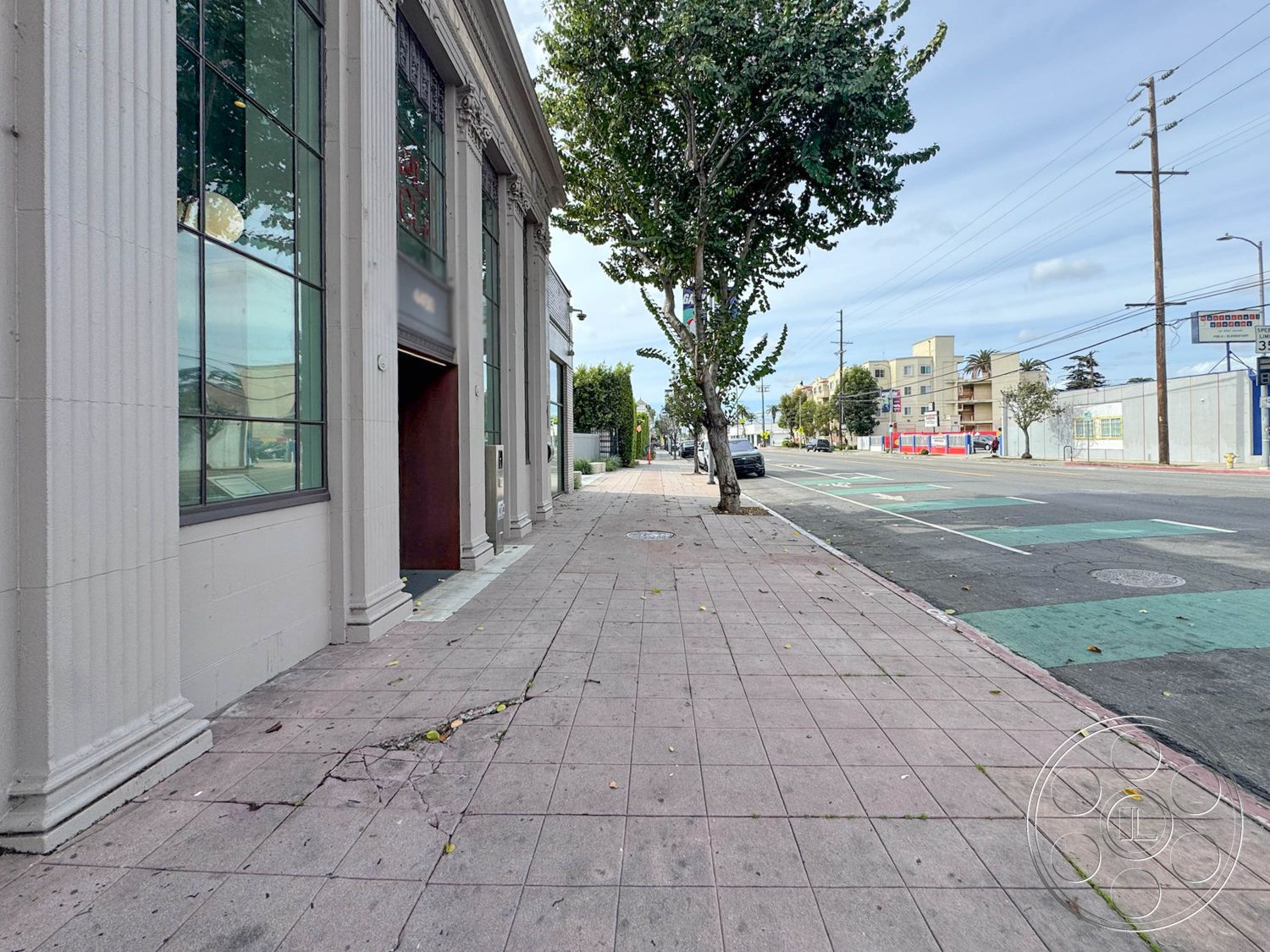 Studio 101 - exterior, landscaped greenery, modern architectural style, city street view, pedestrian pathway, concrete sidewalk, paved street, urban commercial setting, brick building facade, large glass storefront windows, streetlight installations, architectural columns with fluted detailing, metal door entrance, horizontal tree canopy