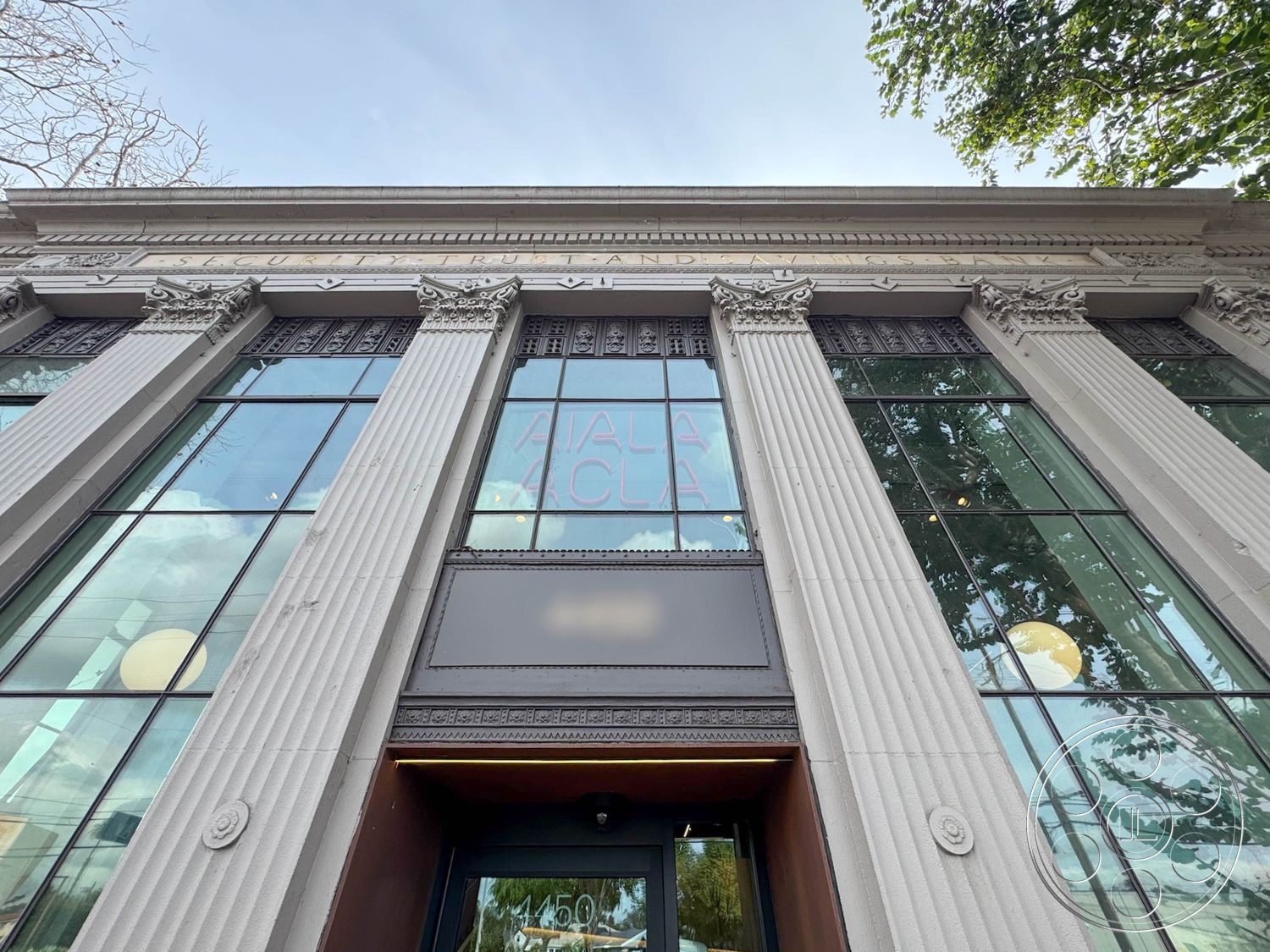 Studio 101 - exterior, large glass windows, urban setting, historical building, columned entrance, symmetrical building design, classical architectural style, ornate stone facade, decorative metal grillwork, engraved stone detailing, high ceilings with detailed cornices, natural light-enhanced entryway, leafy street-side trees, brass door fixtures