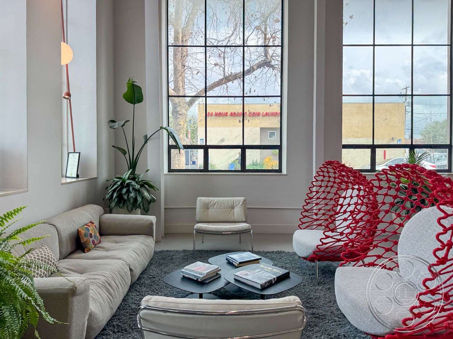 Studio 101 - high ceilings, neutral color palette, textured area rug, light gray wall color, open concept layout, large industrial windows, decorative throw pillows, black round coffee table, interior seating area, natural light flooding in, potted indoor plants, contemporary sectional sofa, minimalist light fixture, modern accent chairs, urban setting view, exposed steel window frames, stacked coffee table books