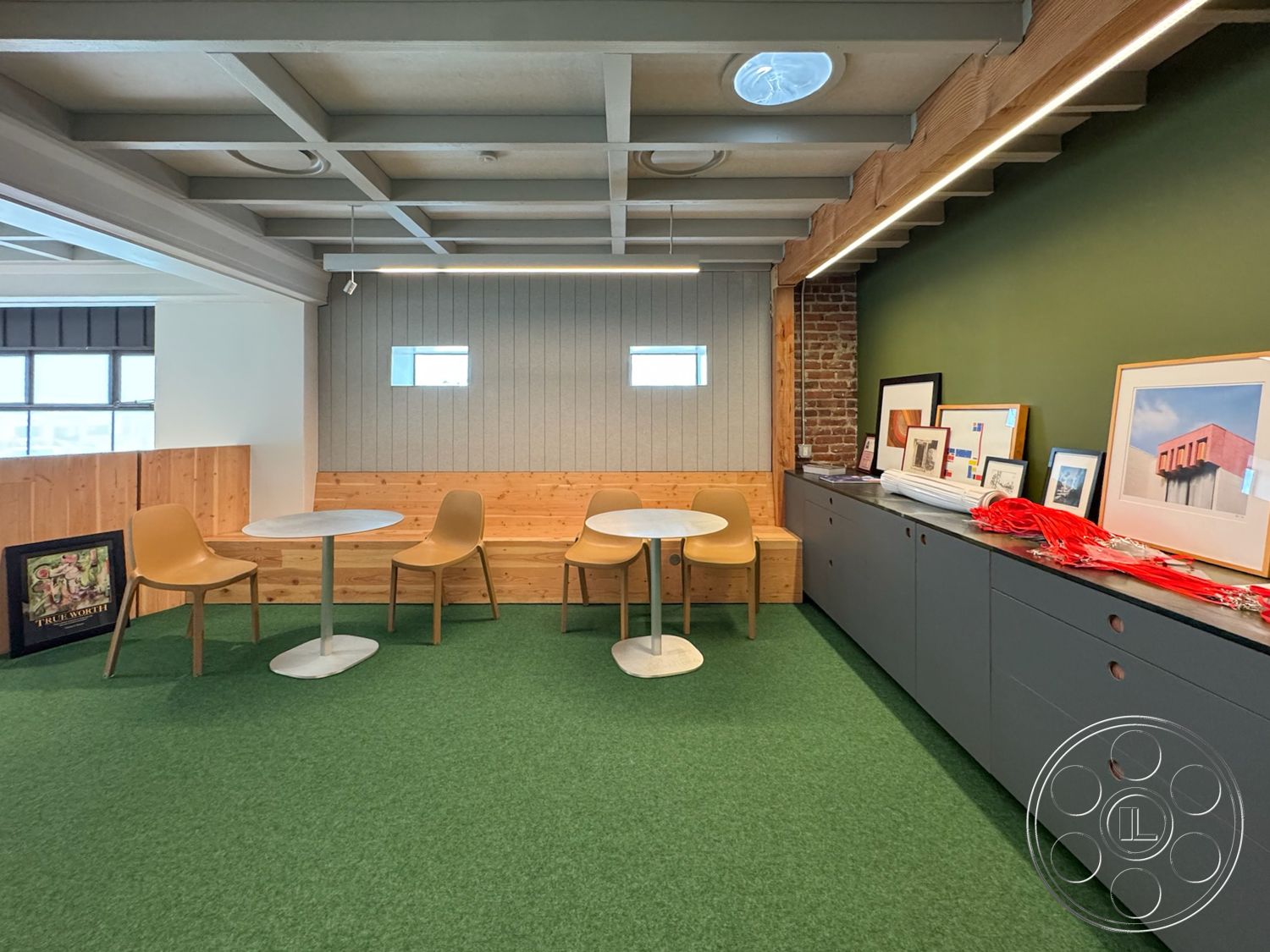 Studio 101 - artwork display, contemporary design elements, linear LED lighting, functional meeting space, round dining tables, flat ceiling with exposed beams, green carpet flooring, green painted walls, exposed brick feature wall, wood paneling seating area, plastic dining chairs