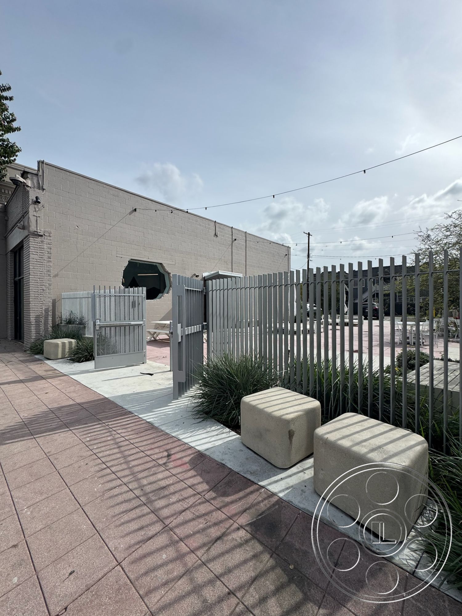 Studio 101 - natural light, exterior, surrounding greenery, urban setting, outdoor lounge area, paved pathway, modern architectural style, textured concrete surface, concrete patio floor, rectangular outdoor space, metal fence with vertical slats, concrete seating blocks, green landscaping with ornamental grasses, light-assembled gate, melange of textures