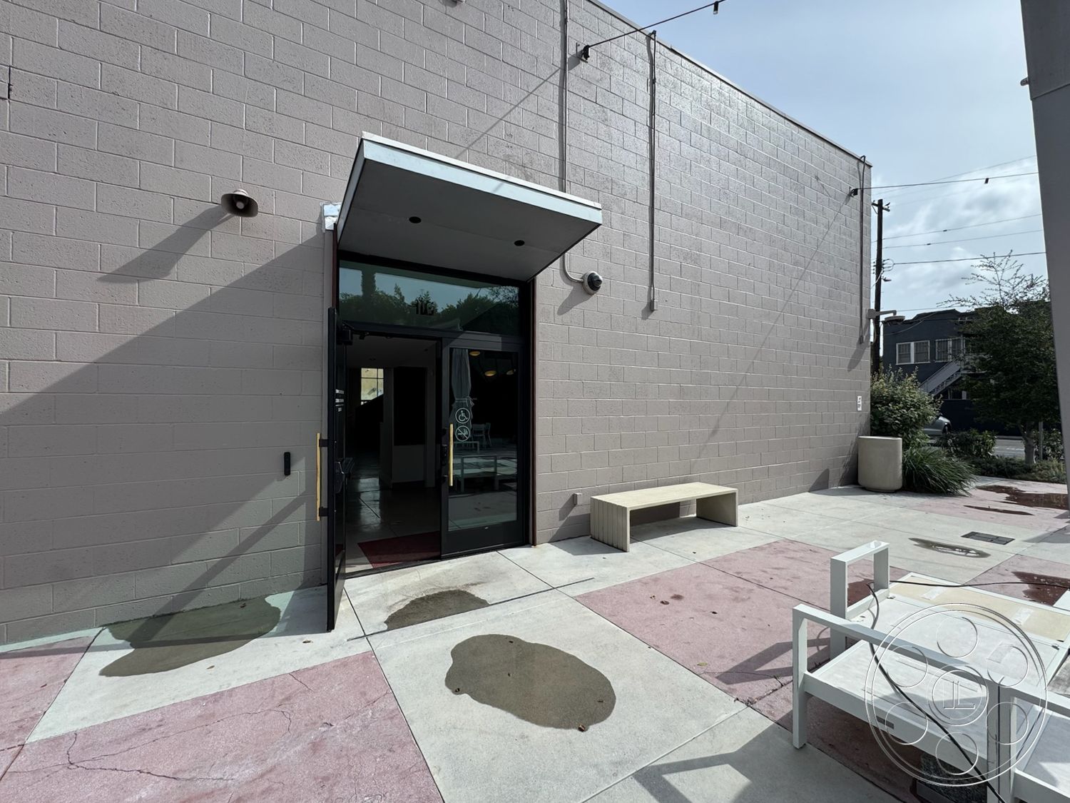 Studio 101 - minimalist design elements, urban environment, landscaped planters, hardscape elements, accessible entrance, concrete patio flooring, modern outdoor seating area, glass entrance door, gray painted walls, natural light entry, exterior concrete block walls, polished concrete surface, string lights for ambiance, rectangular bench seating, casual urban setting