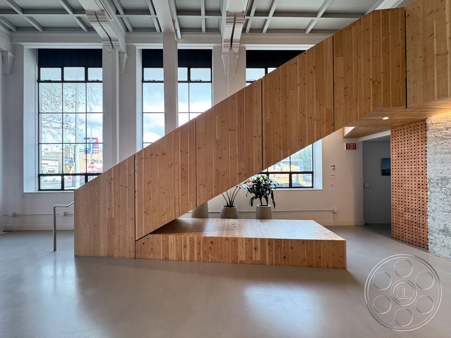 Studio 101 - polished concrete flooring, open concept space, minimalist interior design, concrete floor finish, modern interior finishes, ambient lighting details, textured wood accent wall, exposed wood staircase, spacious interior layout, wood paneling stair details, new industrial aesthetic interior, large steel-framed windows, vaulted ceiling with wood beams, plant decor at entry, natural light infused room, sustainable wood materials, large entry foyer, artistic architectural design, urban contemporary style, functional staircase-integrated seating