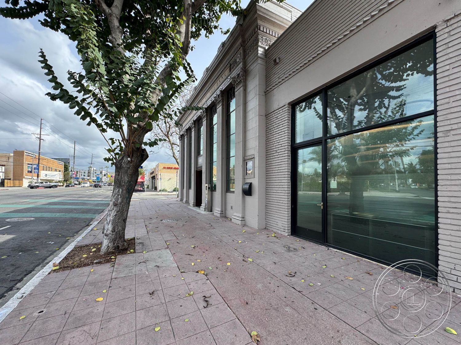 Studio 101 - accessible entryway, concrete sidewalk, textured plaster wall treatment, large glass storefront windows, urban commercial building, mixed-use urban environment, decorative cornice details, exposed brick exterior walls, tree-lined street view, horizontal glass window panels, distressed masonry accents, modern industrial architectural style, single-story building design, public sidewalk setting