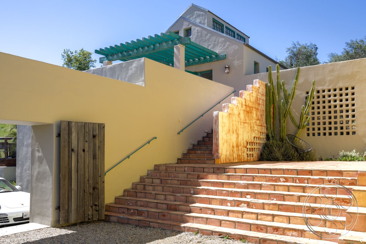 Casa del Rey - exterior, wooden door, metal railing, plastered walls, gravel driveway, urban desert setting, terracotta stair treads, cactus landscaping, green pergola, staggered staircase design, grid pattern wall detail