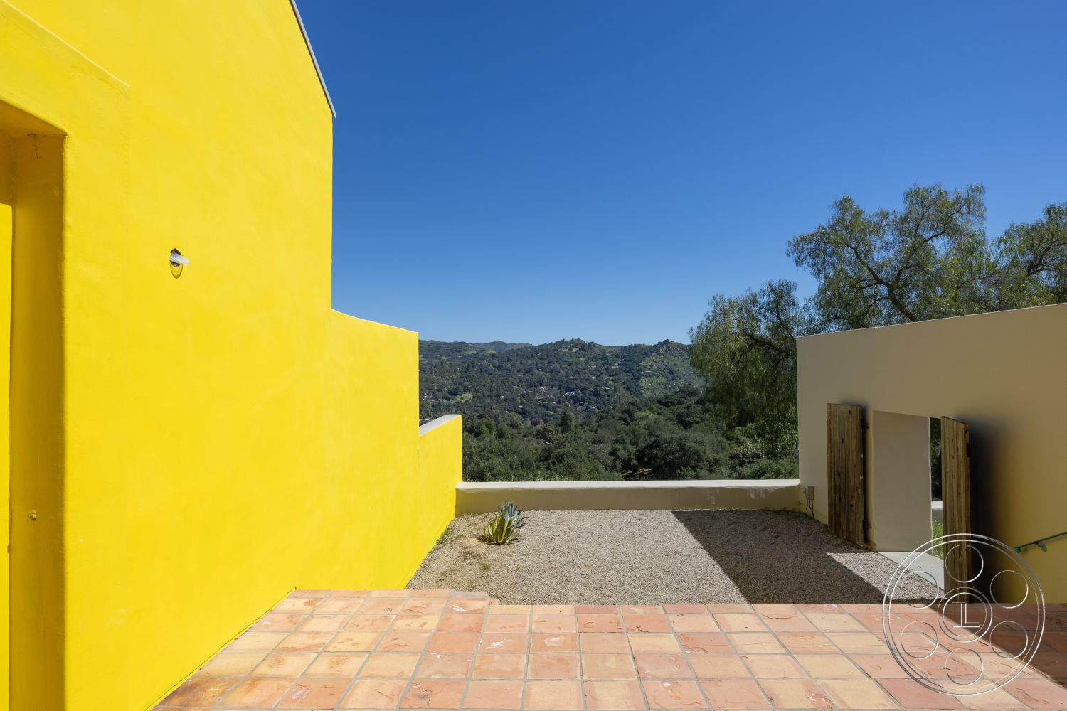 Casa del Rey - open-air terrace, modern architectural design, interior outdoor space, landscaped hillside view, minimalist outdoor setting, wooden door entrance, exterior yellow stucco walls, terracotta tile patio flooring, natural stone gravel ground, smooth finish wall treatments