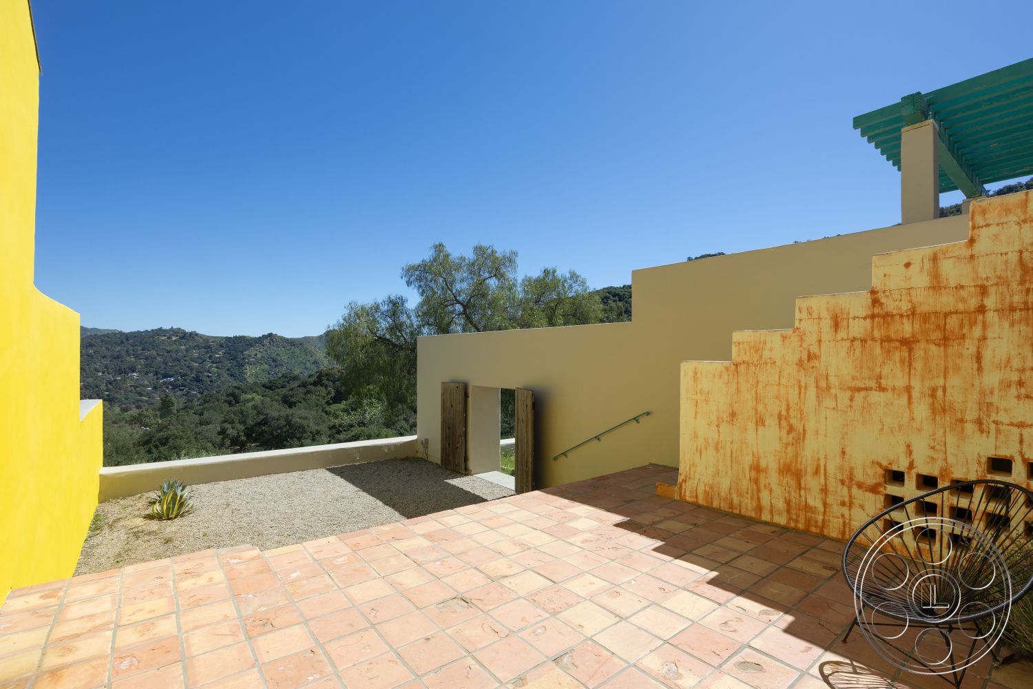 Casa del Rey - outdoor seating area, open-air design, drought-resistant plants, mountain view setting, yellow stucco wall, exterior patio with terracotta tile flooring, unfinished concrete wall, metal door with rustic finish, wooden staircase with a natural finish, green wooden pergola, landscaped area with native plants, casual outdoor ambiance