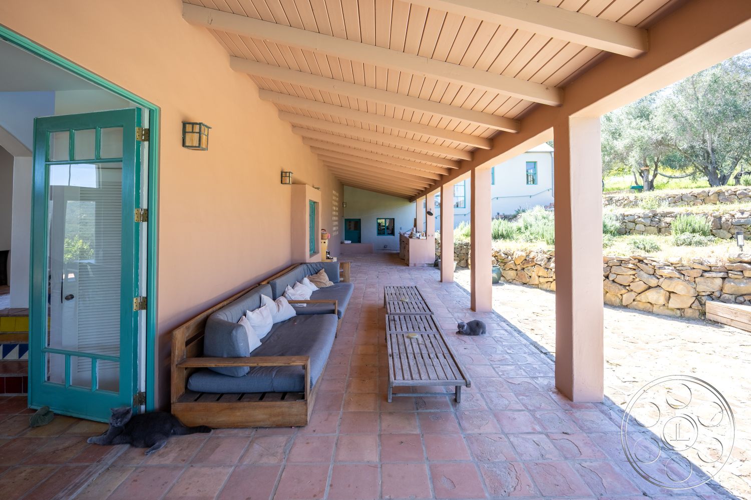 Casa del Rey - arched doorways, decorative wall sconces, terracotta tile flooring, plaster wall finish, open-air layout, wood beam ceiling, potted plant accents, minimalist outdoor furniture, sliding glass door entry, outdoor seating area with cushions, exterior porch area, rustic stone wall background, natural setting with surrounding greenery, urban garden pathway, sunlit shaded porch, cozy lounging space, spacious outdoor area for gatherings