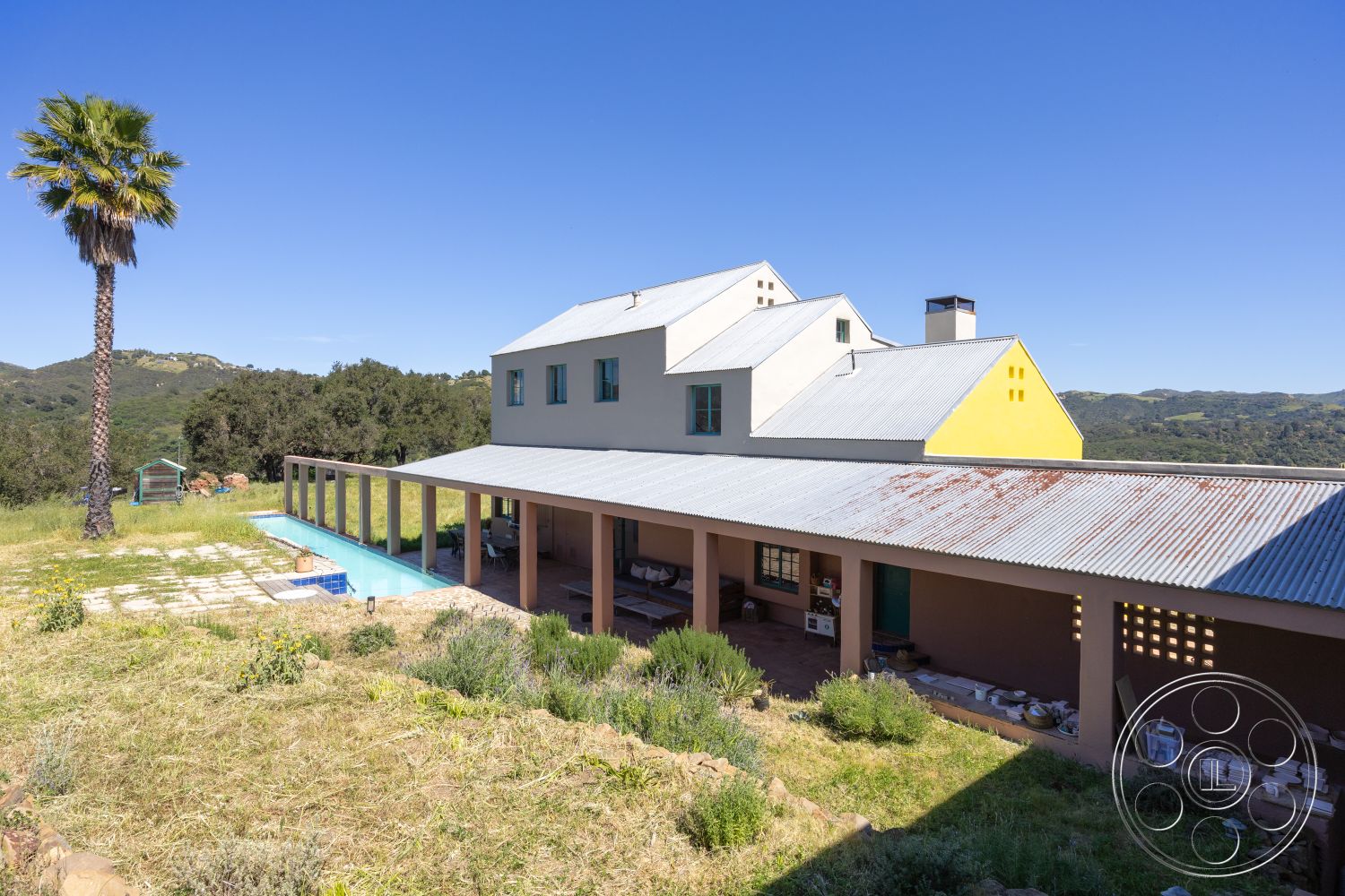 Casa del Rey - rectangular swimming pool, outdoor living space, concrete pool deck, poolside lounging area, mountain view setting, floor-to-ceiling sliding glass doors, landscaped garden with native plants, paved stone patio flooring, exterior painted stucco walls, open-air patio area, metal corrugated roof, exposed wood support beams, brightly colored siding accents, vaulted roofline, lightweight aluminum window frames, green hillside backdrop