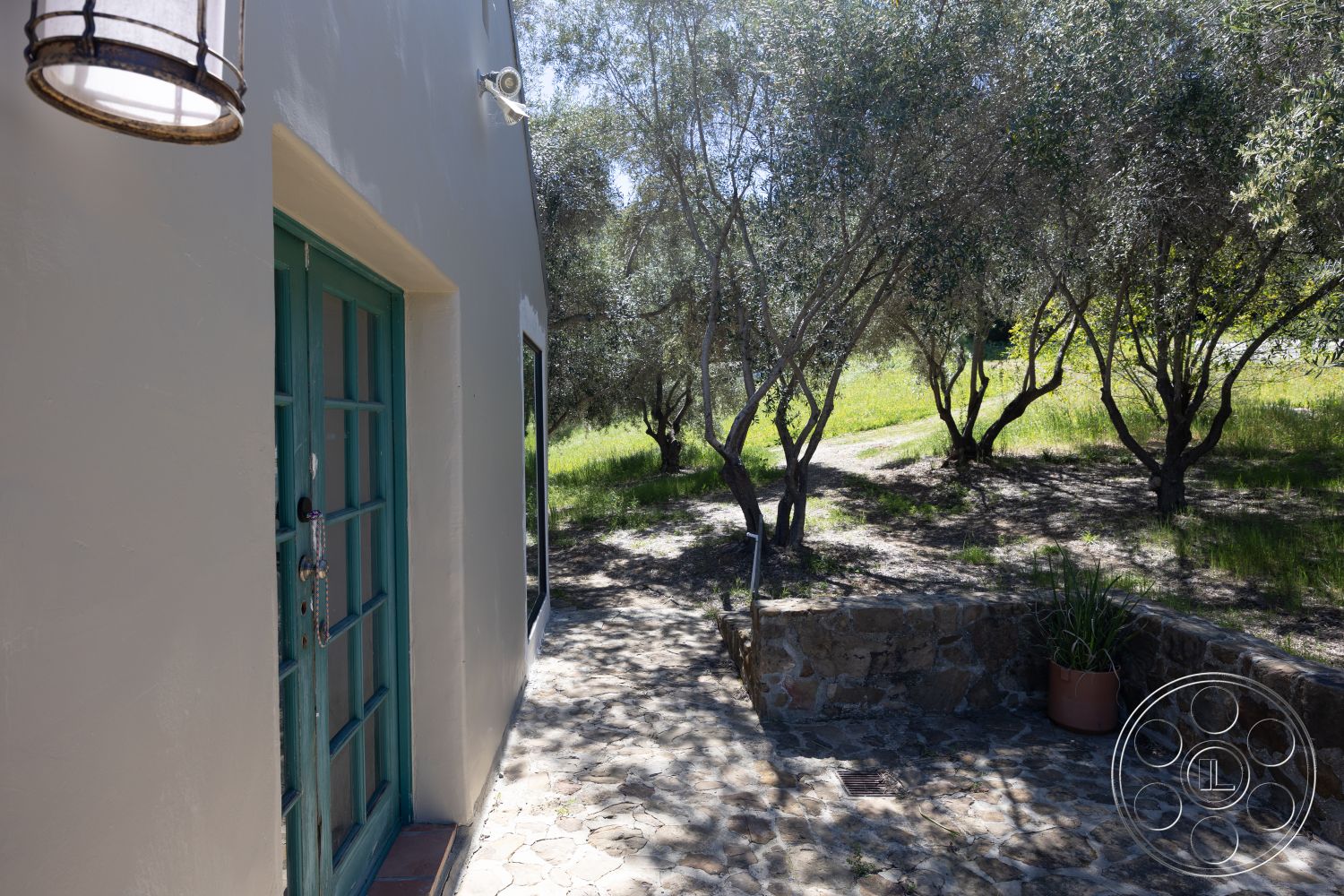 Casa del Rey - exterior, large windows for natural light, textured plaster walls, cobblestone pathway, natural stone retaining wall, blue wood-framed doors, green landscape setting, olive trees surrounding property, modern lantern lighting fixture, view of grassy hillside
