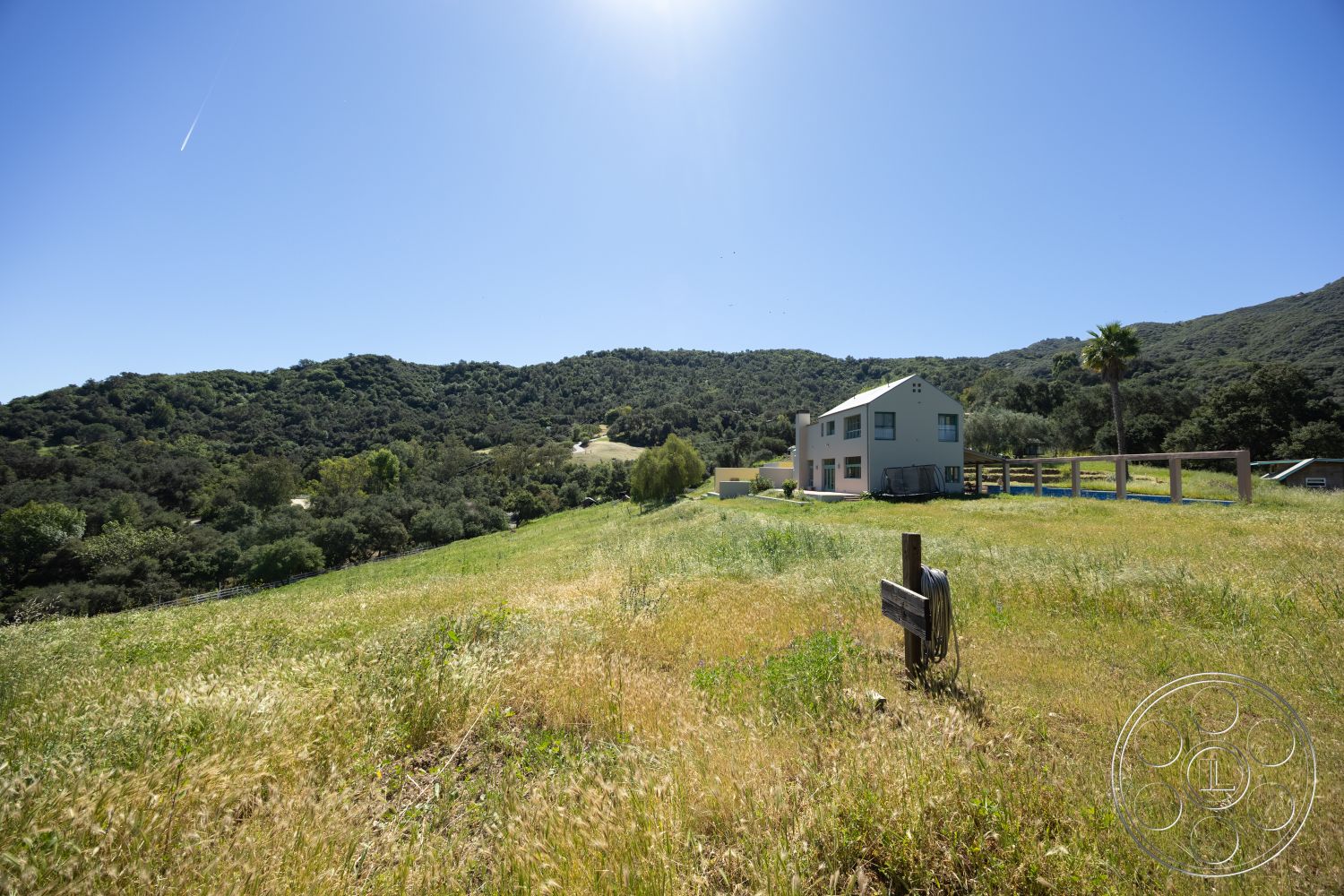 Casa del Rey - modern architectural style, solar panels on roof, exterior hillside location, multiple windows for natural light, exposed concrete foundation, wooden fence posts, two-story contemporary home, open grassy field, palm tree in foreground, metal roof with steep pitch, large front yard with wildflowers, surrounding rolling hills, highland vegetation