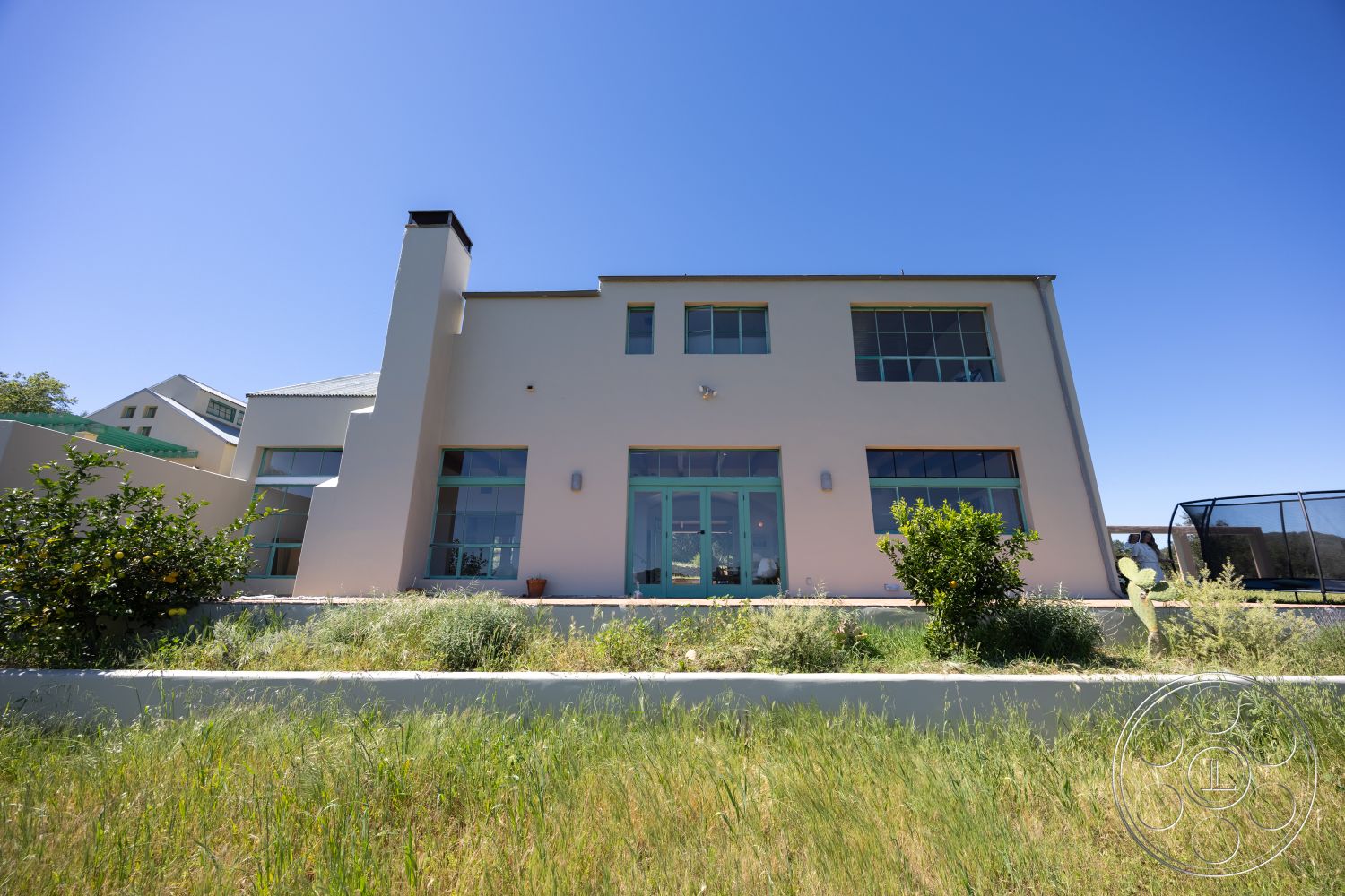 Casa del Rey - landscaped garden, large glass sliding doors, open concept design, modern architectural style, rectangular windows, flat roof design, urban hillside location, stucco exterior walls, concrete foundation, natural sunlight exposure, green grass landscaping, exterior light fixtures, spacious patio area, minimalist house facade, metal roof accents