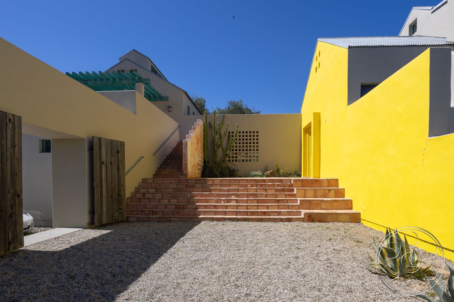 Casa del Rey - exterior, modern architecture, paved walkway, minimalist landscaping, yellow stucco walls, wooden gate, open-air environment, natural light exposure, Bohemian, gravel courtyard, desert plant landscaping, geometric building shapes, rectangular stair design, green pergola, brick outdoor stairs, textured surface walls