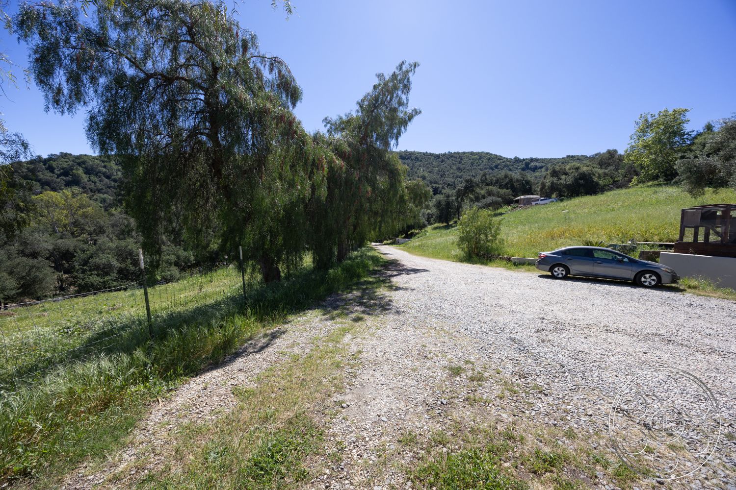 Casa del Rey - exterior, mountain view, clear blue sky, gravel driveway, surrounded by trees, open grassy area, natural landscape setting, rural location, ground-level parking area, scenic drive