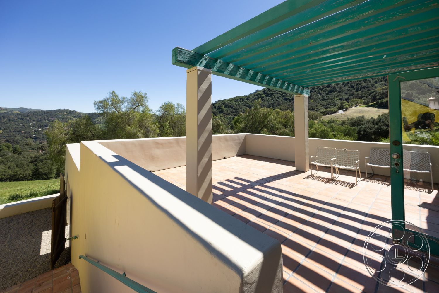 Casa del Rey - sunny outdoor space, mountain view setting, natural light exposure, landscaped hillside environment, exterior terrace with clay tile flooring, stucco walls with neutral paint finish, wooden pergola with turquoise beams, open outdoor seating area with metal chairs, spacious terrace for entertaining, roller door access from the garden, interior access door with glass panel, sloped topography