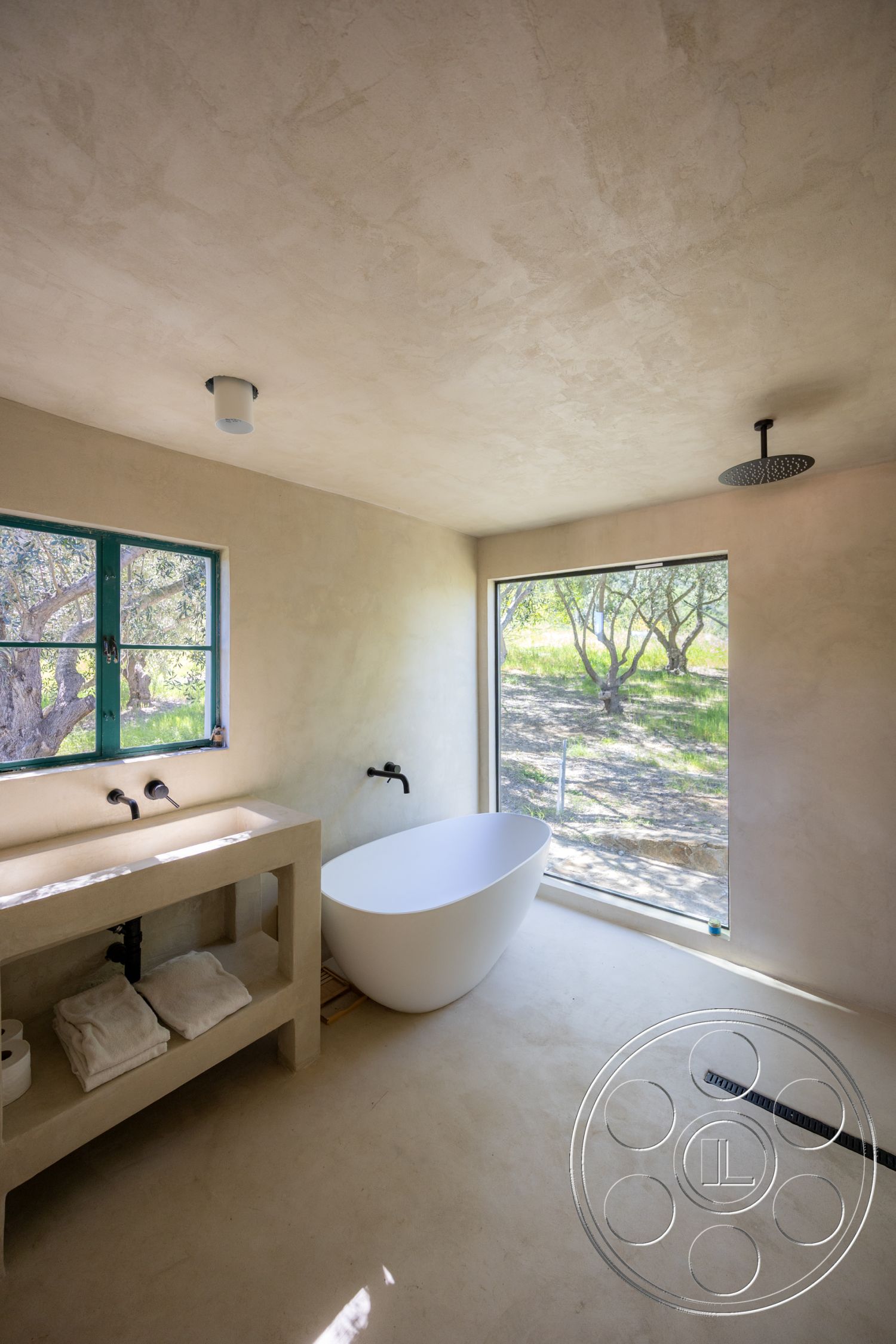 Casa del Rey - neutral color palette, natural light, minimalist design, open space layout, greenery view, sconce lighting, textured plaster walls, large floor-to-ceiling windows, interior bathroom, freestanding white bathtub, concrete sink vanity, black wall-mounted faucets, modern fixture