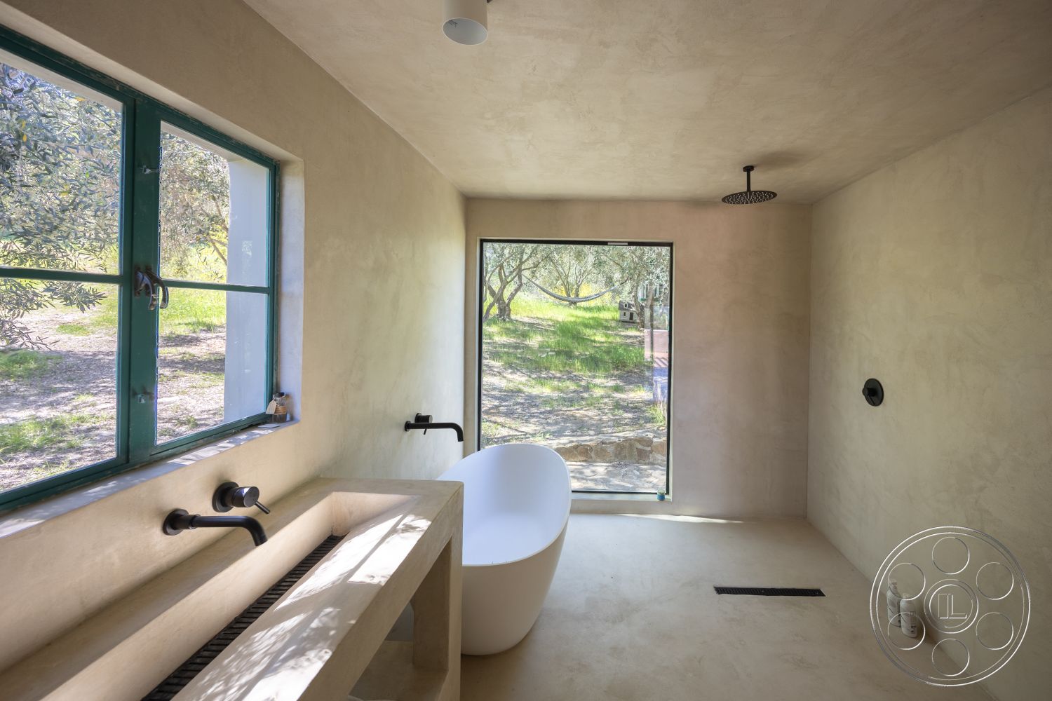 Casa del Rey - neutral color palette, smooth concrete flooring, textured plaster ceiling, large floor-to-ceiling windows, natural light setting, modern minimalist design, freestanding oval bathtub, simple pendant lighting, spacious open layout, green framed windows, interior bathroom with plastered walls, concrete sink unit, minimalist shower fixture, open olive grove view