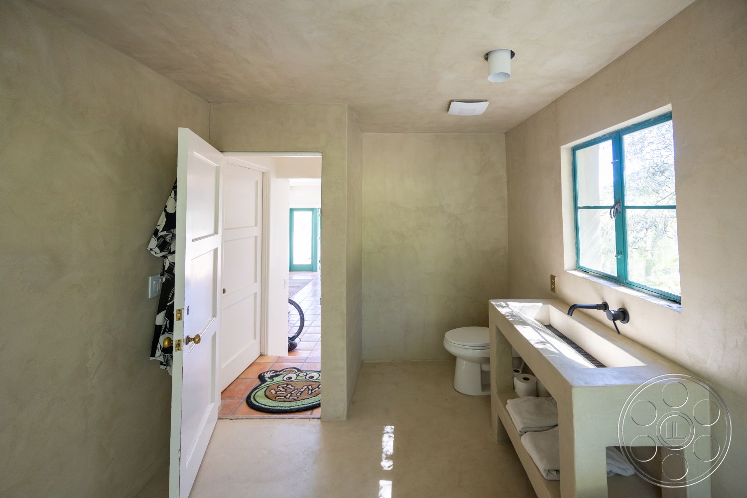 Casa del Rey - neutral color palette, natural light from window, concrete bathroom flooring, functional bathroom design, interior bathroom with textured plaster walls, modern farmhouse door, vintage green window frames, minimalist open space layout, simple wall-mounted faucet, clean lines in bathroom design, spacious layout with direct access, stylish entryway with rustic flooring