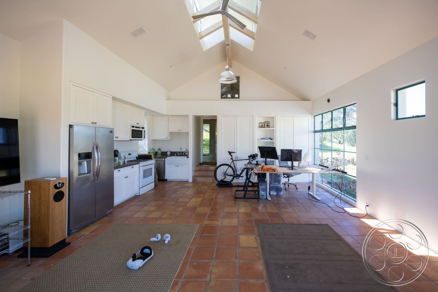 Casa del Rey - contemporary design, minimalist aesthetic, multifunctional space, modern pendant lighting, floor-to-ceiling windows, accessible layout, stainless steel kitchen appliances, open-concept living area, vaulted ceiling with exposed wood beams, natural light abundance, terra cotta tile flooring, neutral wall treatment, white shaker kitchen cabinets, modern home office setup, bicycle storage area, cozy living corner, casual living environment, views of green landscape, outdoor connection through large windows