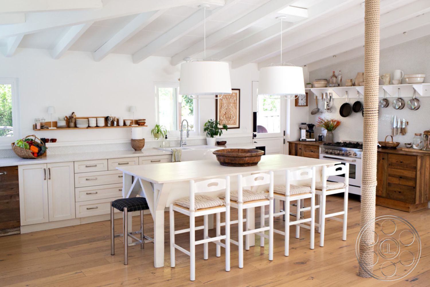 Ranch 33 - minimalist decor, stainless steel appliances, woven bar stools, wood dining table, large windows for natural light, white cabinetry, modern farmhouse style, pendant lighting fixtures, marble kitchen countertop, wood beam ceiling, open concept interior, kitchen island with seating, shiplap kitchen walls, hardwood kitchen floor, exposed wood column, shelving with kitchen essentials