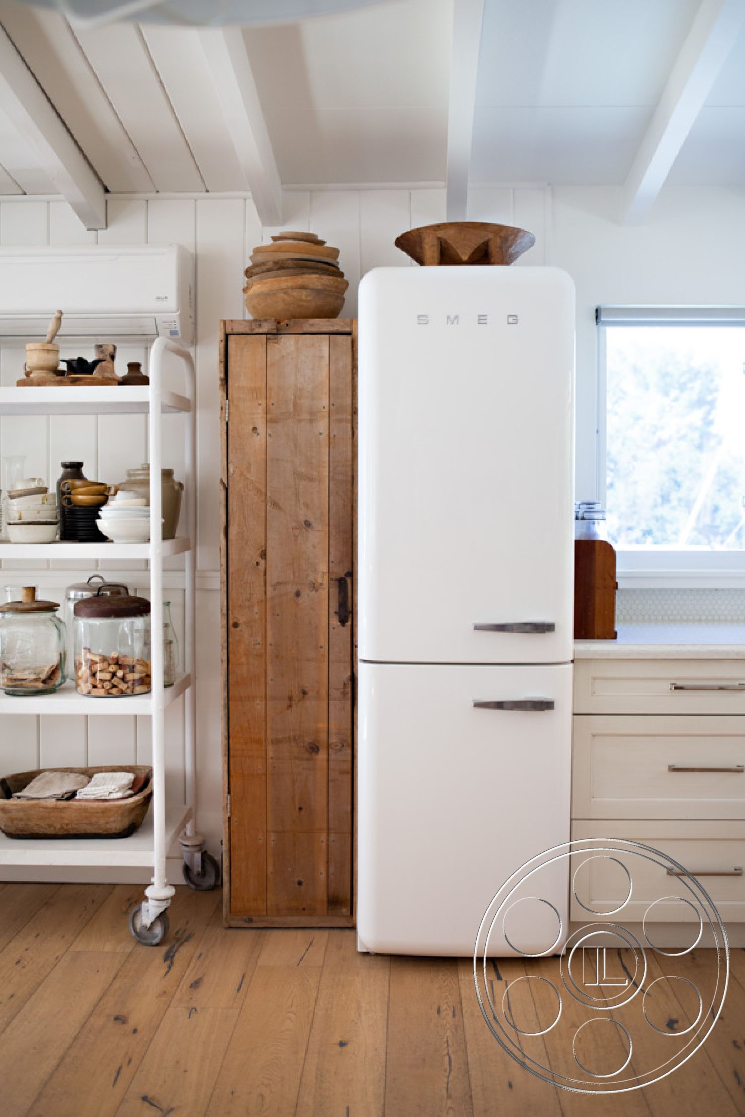 Ranch 33 - textured wall paneling, functional kitchen layout, interior kitchen space, minimalist kitchen design, hardwood kitchen floors, exposed wooden ceiling beams, neutral color palette kitchen, natural light-filled kitchen, white Shaker-style kitchen cabinets, SMEG retro refrigerator, rustic wooden storage cabinet, open shelving with glass jars, country style kitchen, kitchen with vintage decor, wooden bowl kitchen decor