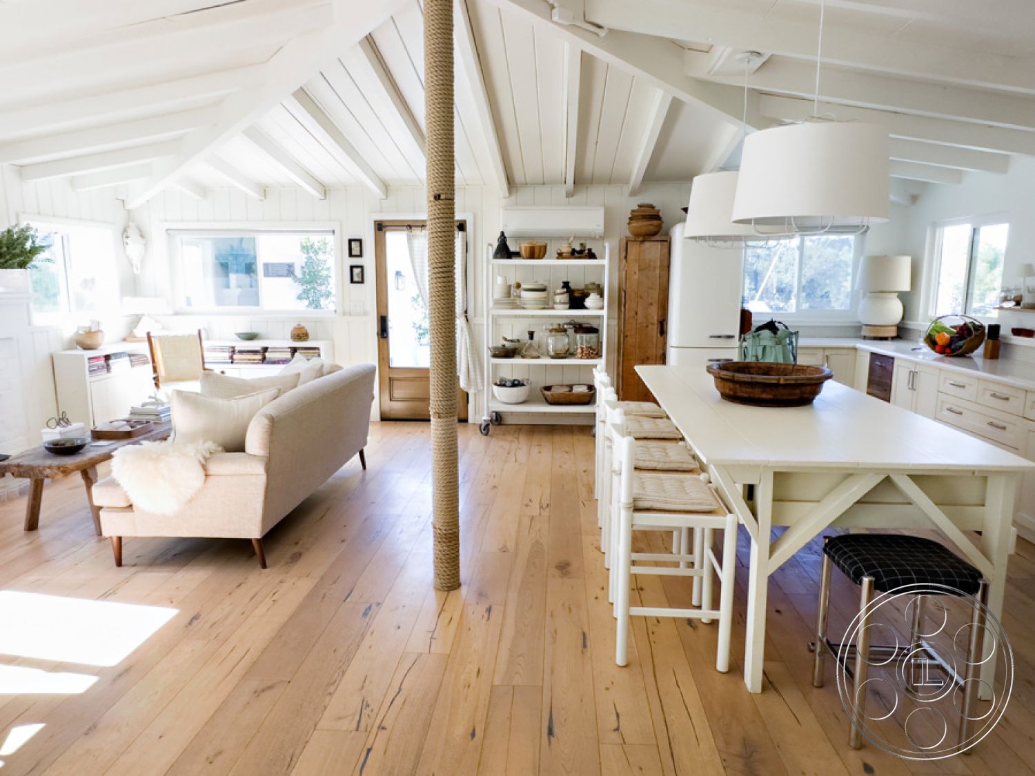 Ranch 33 - neutral color palette, white shiplap walls, exposed wood ceiling beams, interior hardwood living room floors, minimalist decor accents, open concept living area, natural wood shelving unit, rustic wooden coffee table, woven rattan dining chairs, lightly distressed wooden dining table, glass windowpanes with natural light, cozy seating area with sectional sofa, kitchen with modern cabinetry, textured wool throw, functional and bright kitchen space