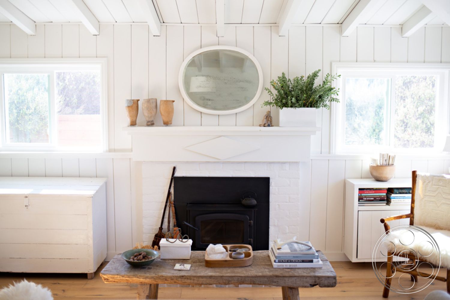 Ranch 33 - exposed wood ceiling beams - interior, neutral color palette - interior, white shiplap walls - interior, black wood-burning stove - interior, natural wood coffee table - interior, wooden storage chest - interior, large round mirror - interior, green potted plant - interior, large windows - interior, textured beige upholstery chair - interior, minimalist decor accessories - interior, rustic farmhouse style - interior, open living space - interior, bright natural light - interior