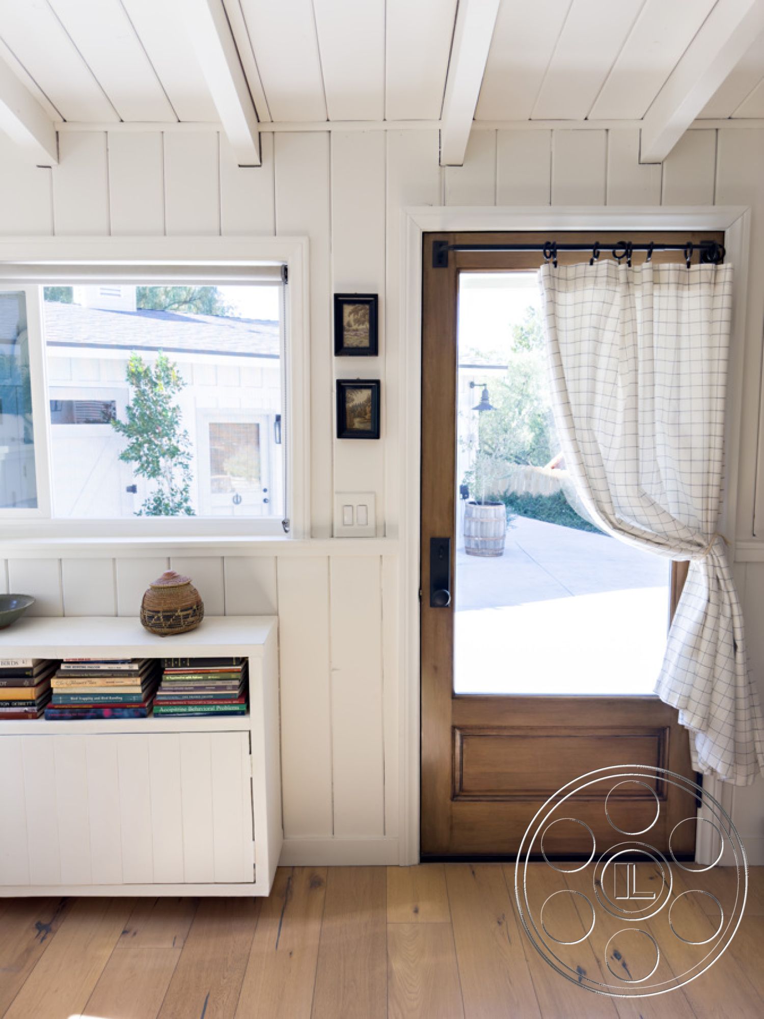 Ranch 33 - light hardwood flooring, floor-to-ceiling windows, white shiplap walls, modern farmhouse style, wooden front door, simple geometric shapes, minimalist decor elements, natural light entry, built-in storage cabinet, textured curtain treatment, open door entryway, decorative book arrangement