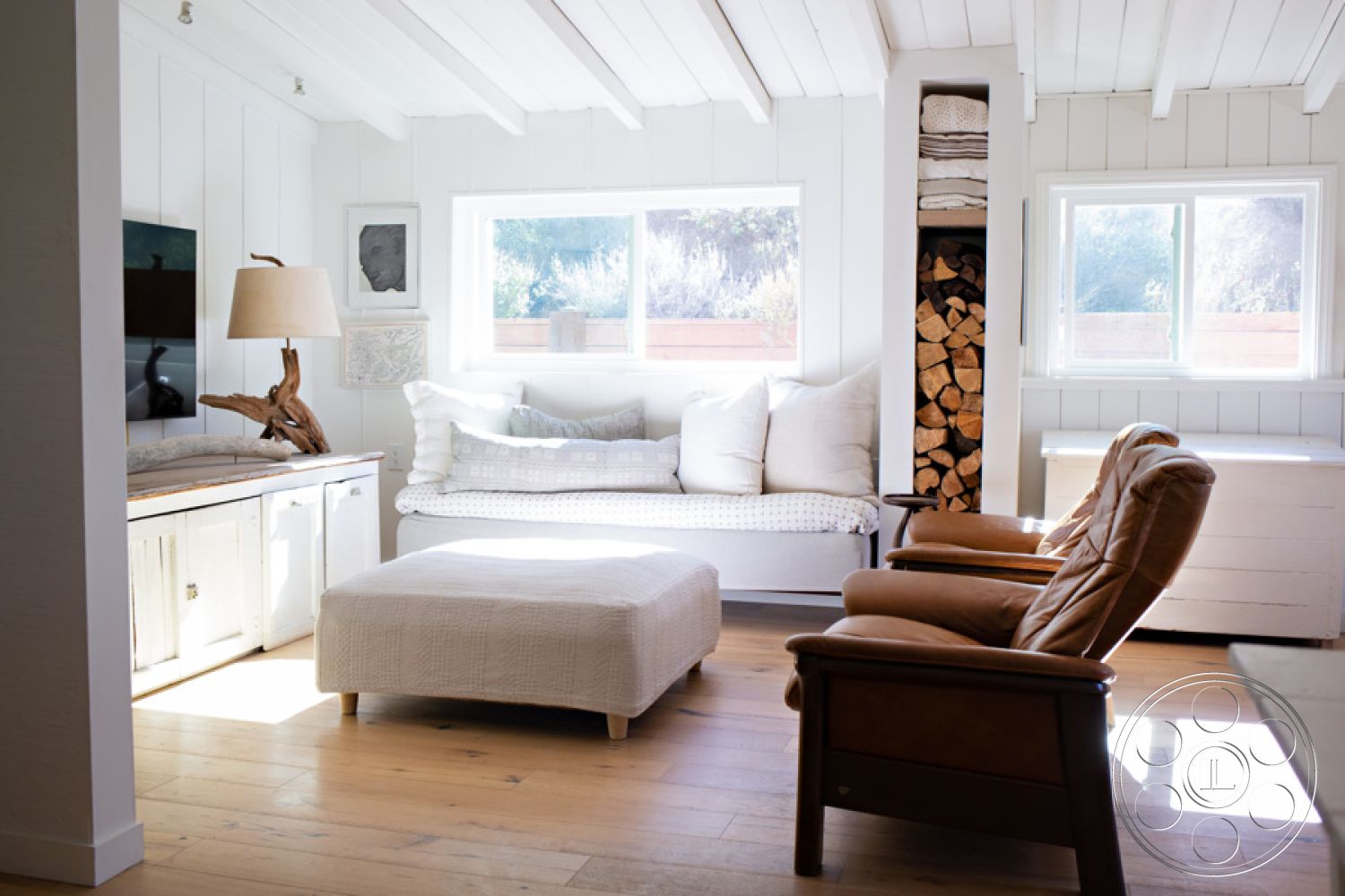 Ranch 33 - neutral color palette interior, open floor plan interior, modern lounge seating interior, natural light flooding interior, minimalist decor interior, hardwood flooring living room interior, wood ceiling beams interior, textured throw pillows interior, white shiplap walls interior, natural wood accent furniture interior, oversized plush ottoman interior, large double-hung windows interior, wooden fireplace wood storage interior, earthy color scheme interior