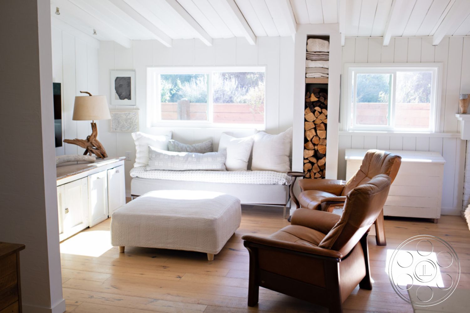 Ranch 33 - exposed wood ceiling beams, white shiplap accent walls, textured plaster interior walls, beige hardwood living room floors, large picture windows with natural light, custom built-in wood storage, cozy reading nook with cushions, simple fabric ottoman, brown leather armchairs, bright, airy interior space, scandinavian-inspired design elements, natural light-filled atmosphere