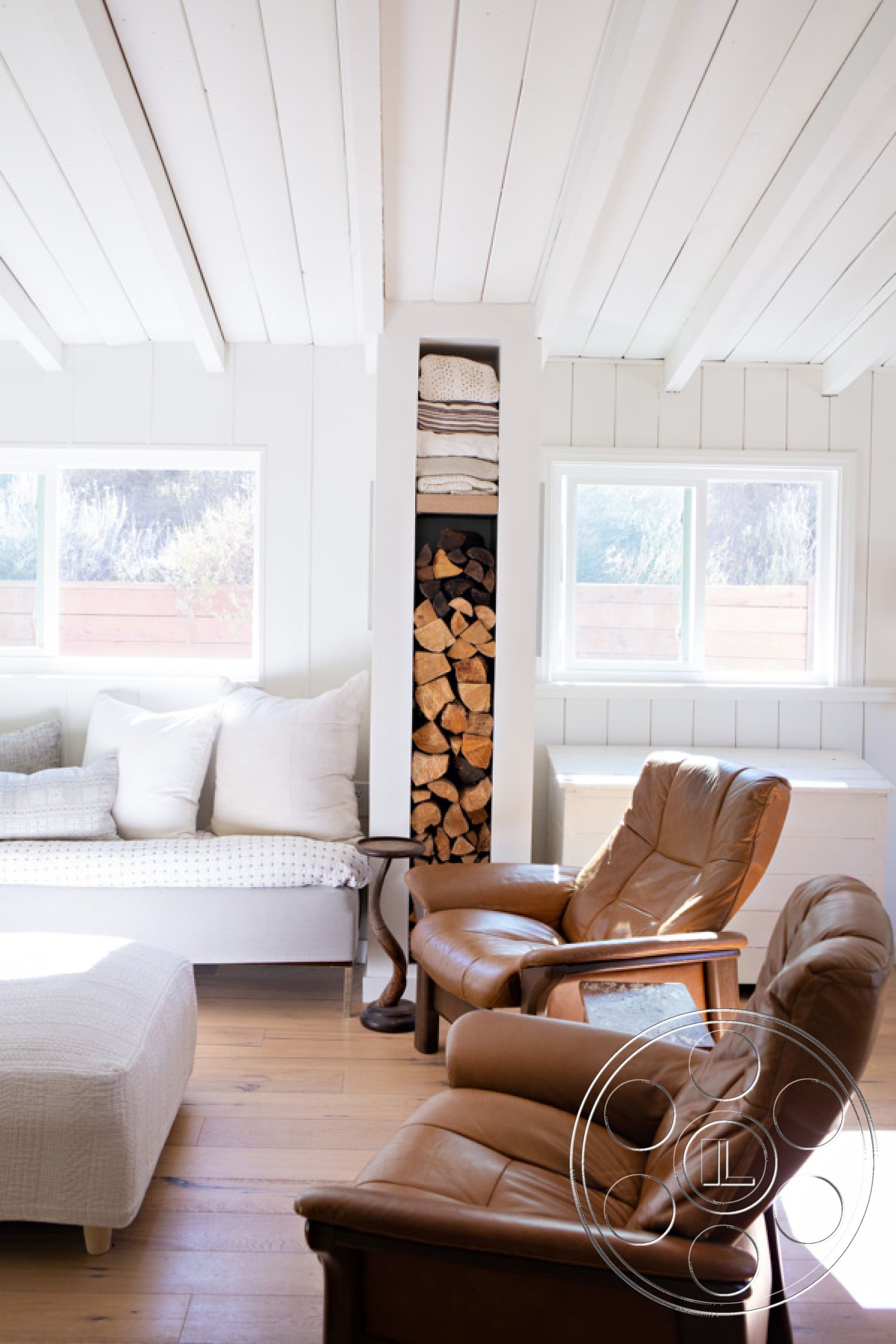 Ranch 33 - interior minimalist decor, interior hardwood living room floors, interior vaulted ceiling with exposed wooden beams, interior cozy seating area, interior large windows for natural light, interior modern accent chairs, interior white shiplap walls, interior wood log storage unit, interior neutral-colored throw pillows, interior simple cream ottoman, interior light wood furniture, interior soft textiles for comfort