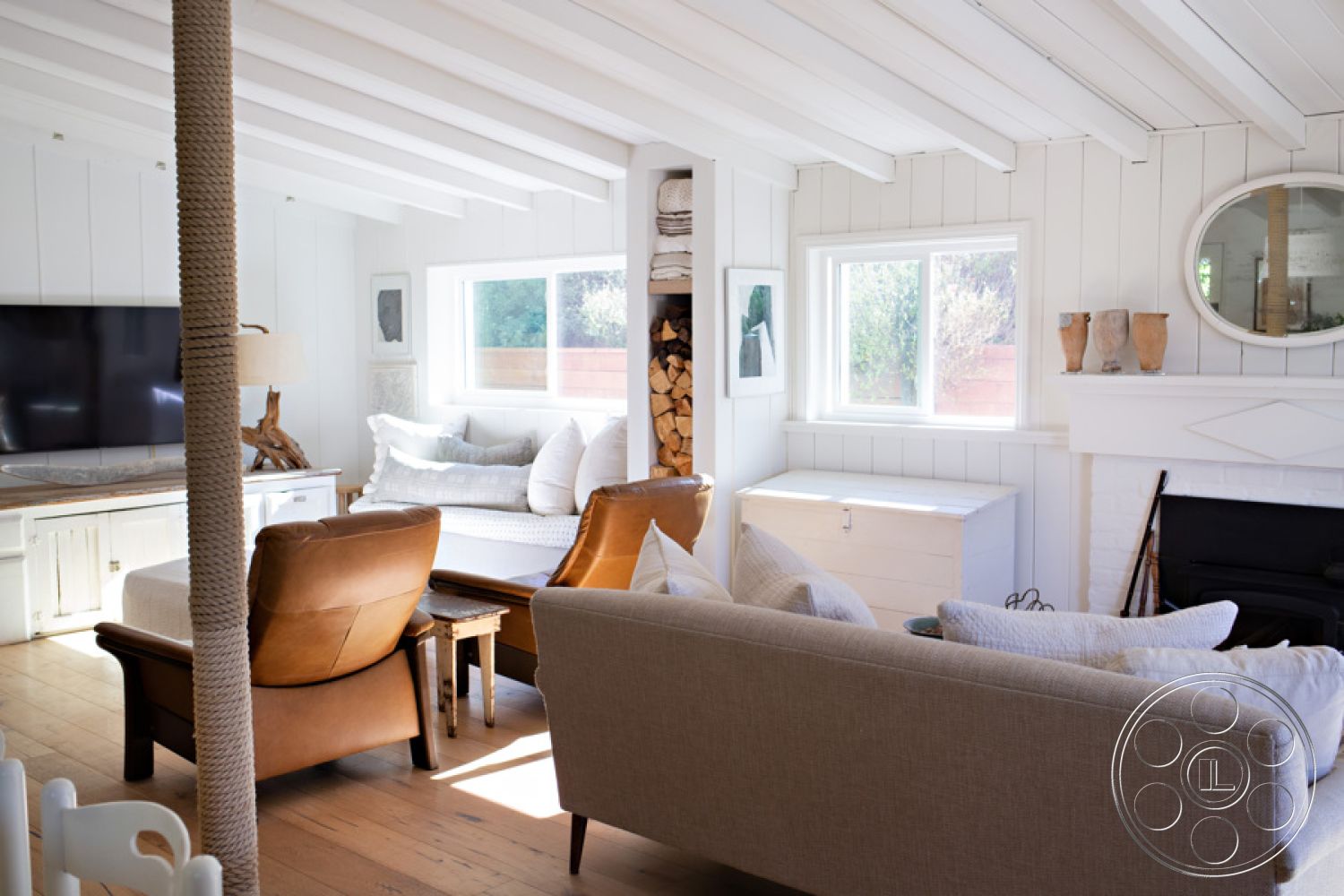 Ranch 33 - soft neutral color palette, white shiplap walls, comfortable sectional sofa, natural light from large windows, cozy reading nook, mid-century modern style, exposed wood ceiling beams, hardwood living room floors, light-filled interior, textured fabric throw pillows, curved accent chair, built-in storage with firewood, wood coffee table with rustic finish, modern flat-screen television mount, wooden decorative accents